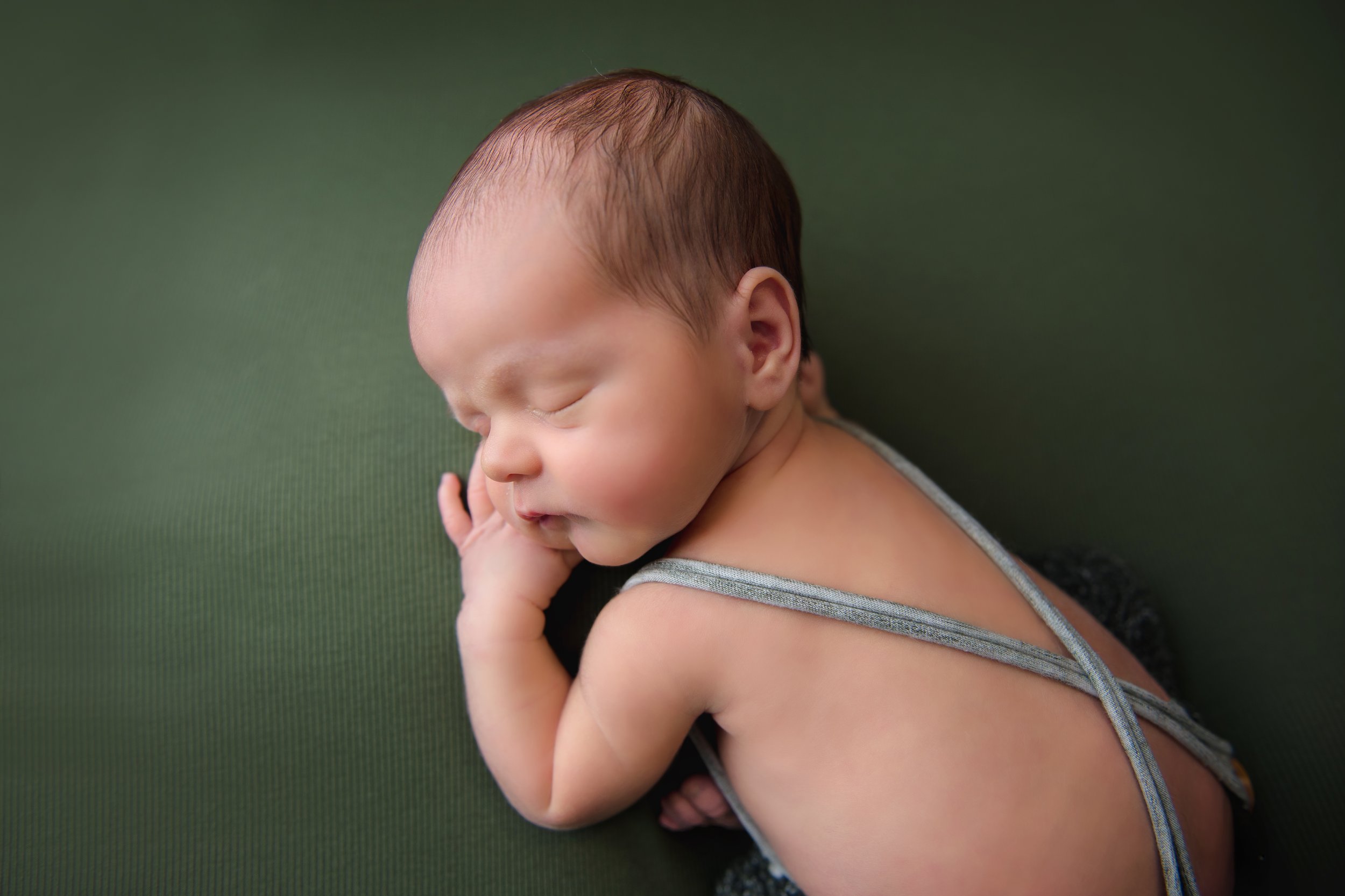 A sleeping newborn baby lying on a green surface, with the head turned to the side and one hand near the face.