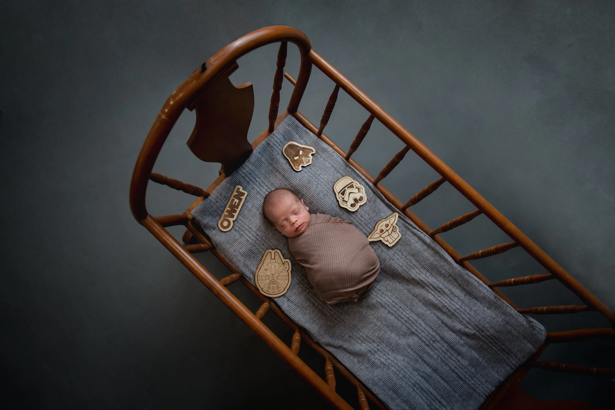 A newborn baby sleeping on a blanket in a wooden crib surrounded by Star Wars themed wooden decorations.