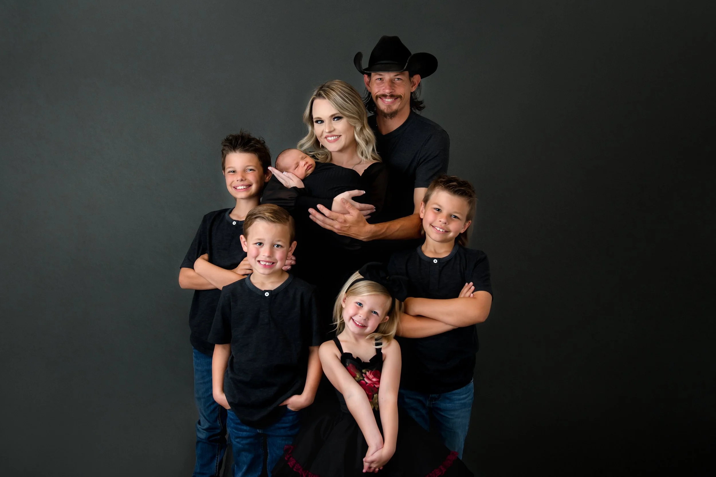 Family portrait of two adults and six children standing against a dark backdrop.
