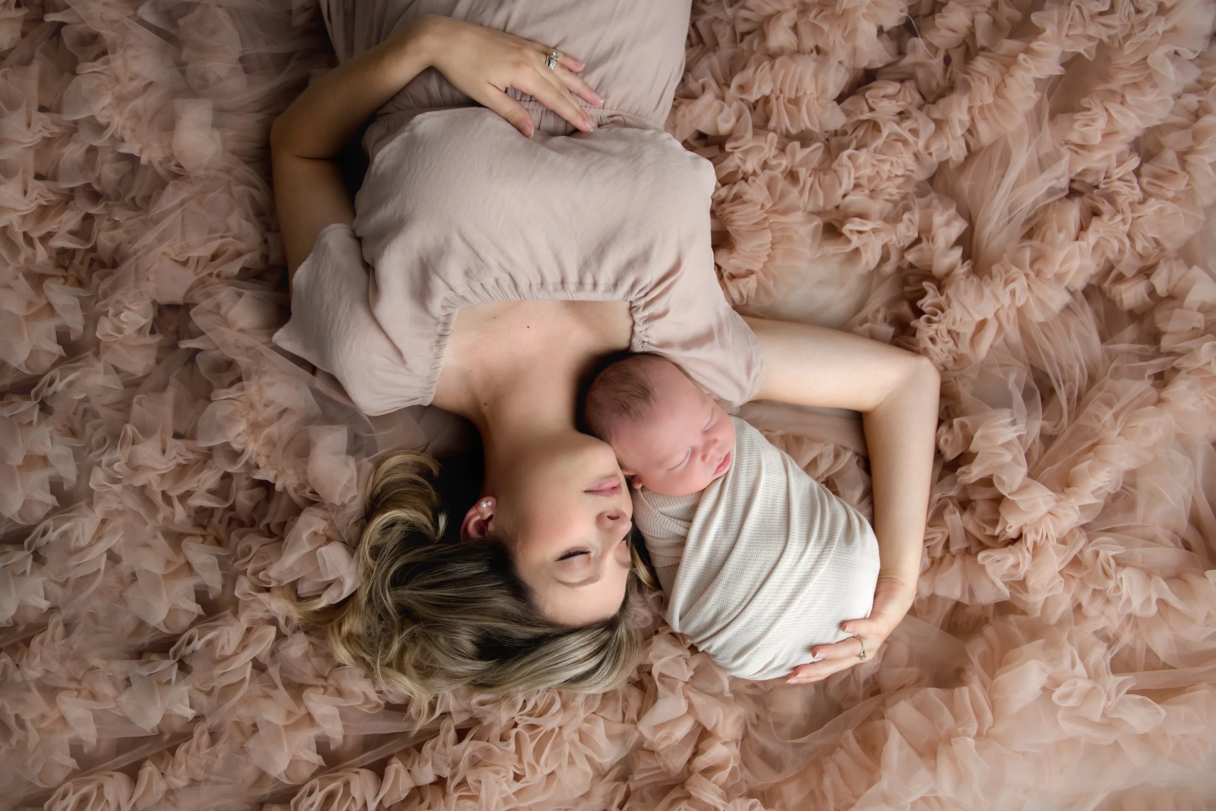 In our Spring Branch studio a woman and a baby sleeping on a ruffled pink blanket, with the woman lying on her side and the baby cuddled close to her head.