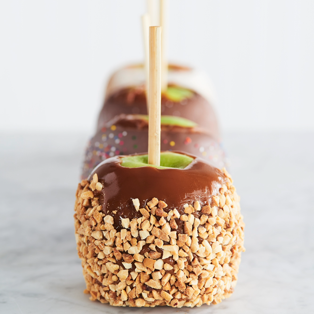 A row of scrumpious chocolate covered apples, dipped in crushed peanuts