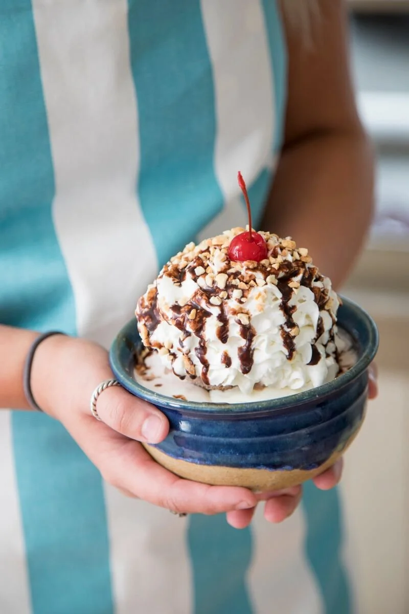 Closeup of customer holding a decadent ice cream sundae drizzed in chocolate and topped with whipped cream