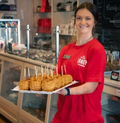 Out shop attendant proudly holds a tray of freshly made chocolate-covered apples