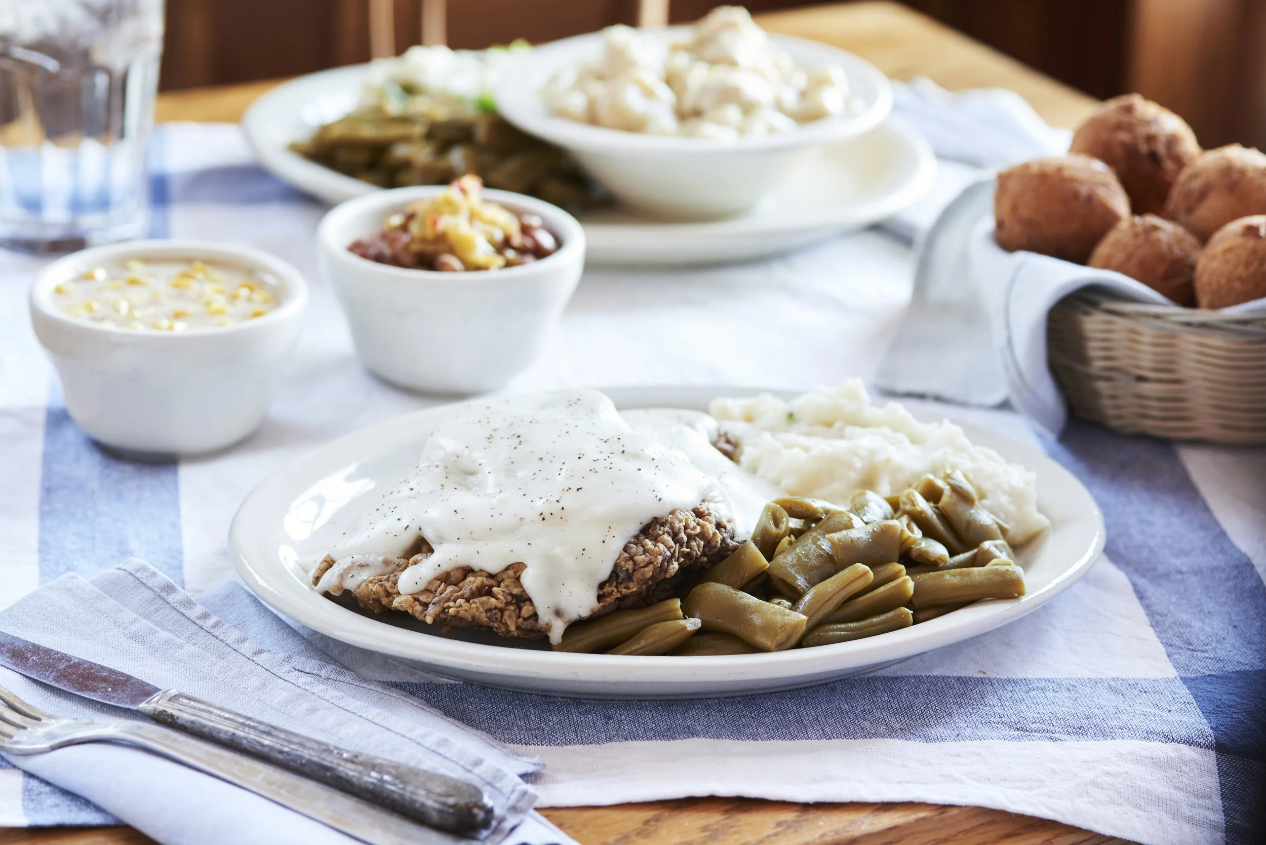 Chicken Fried Steak with gravy, green beans, and mashed potatoes with fritters, beans and corn chowder in the background