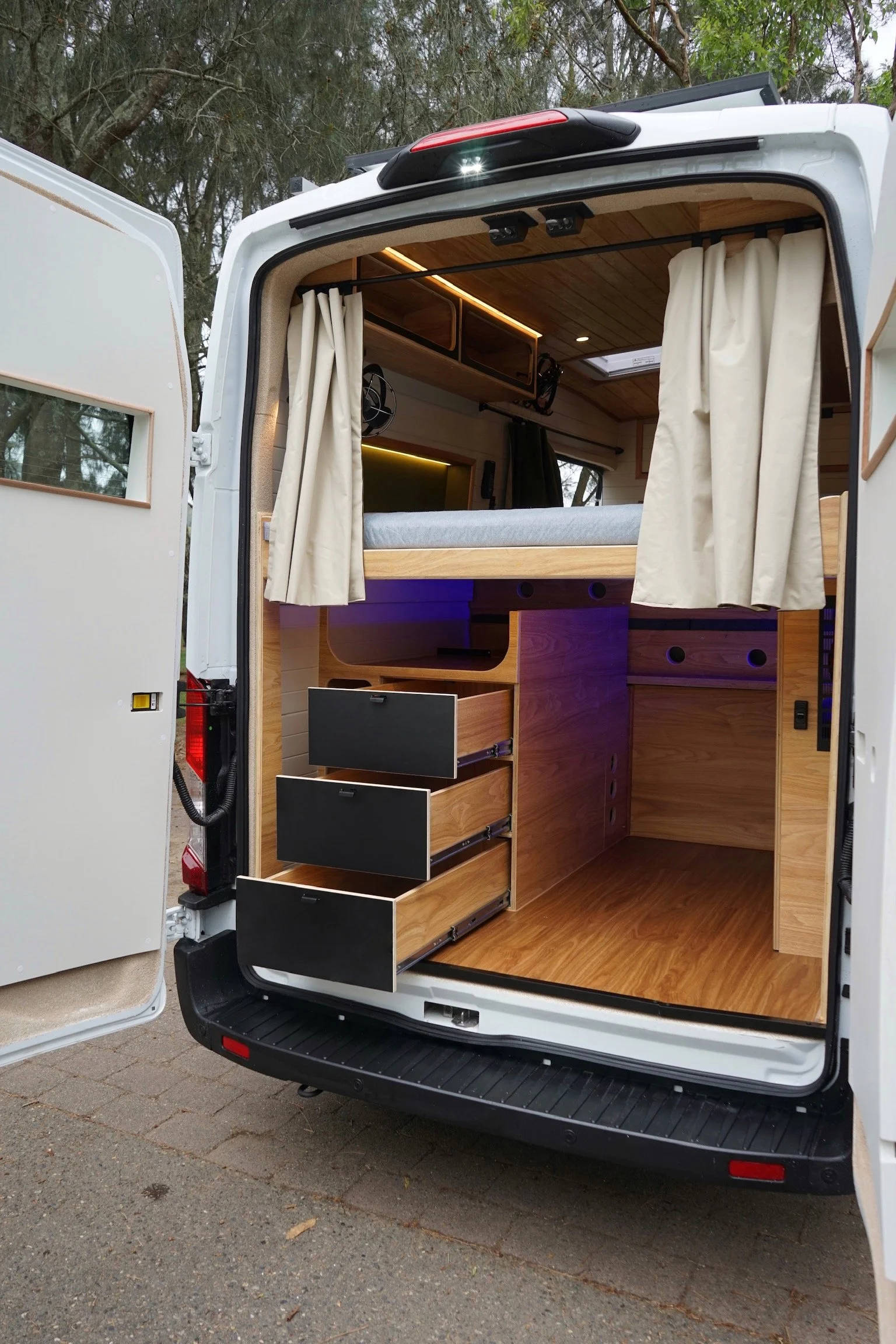 Ford Transit campervan conversion with rear storage drawers, timber cabinetry, bed platform and curtains