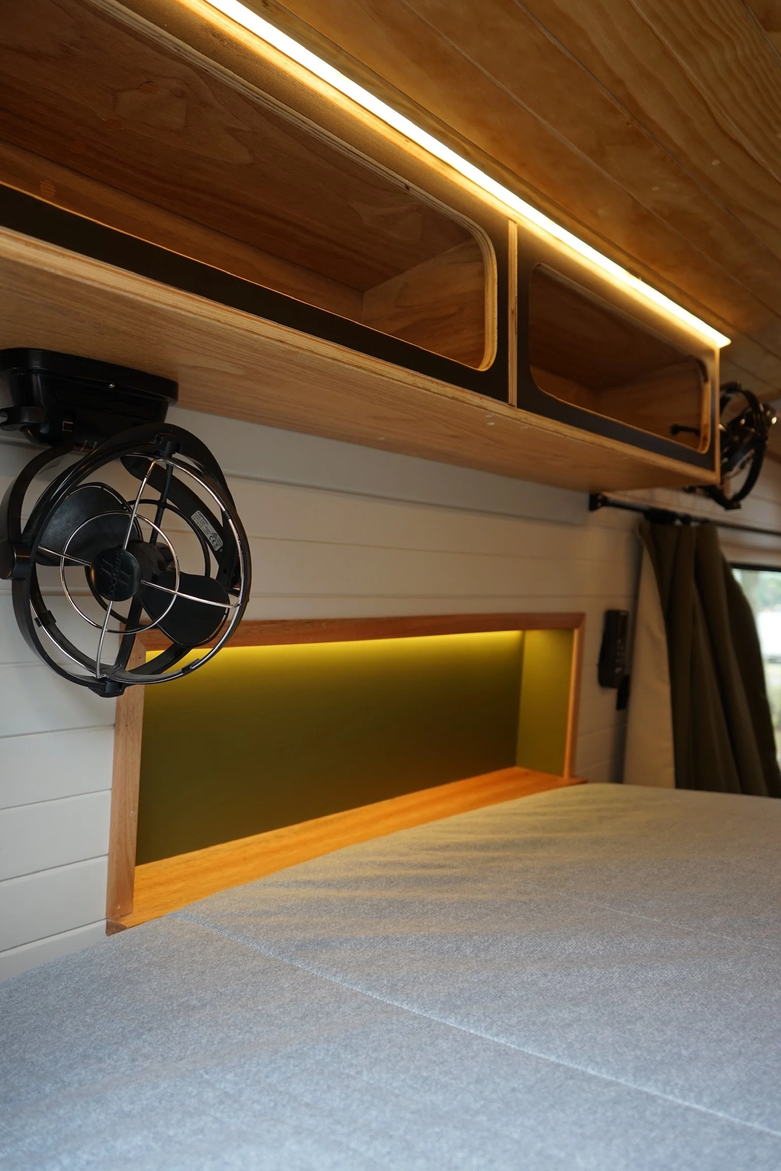 Ford Transit campervan interior with overhead storage, bed area, reading light and custom timber finishes.
