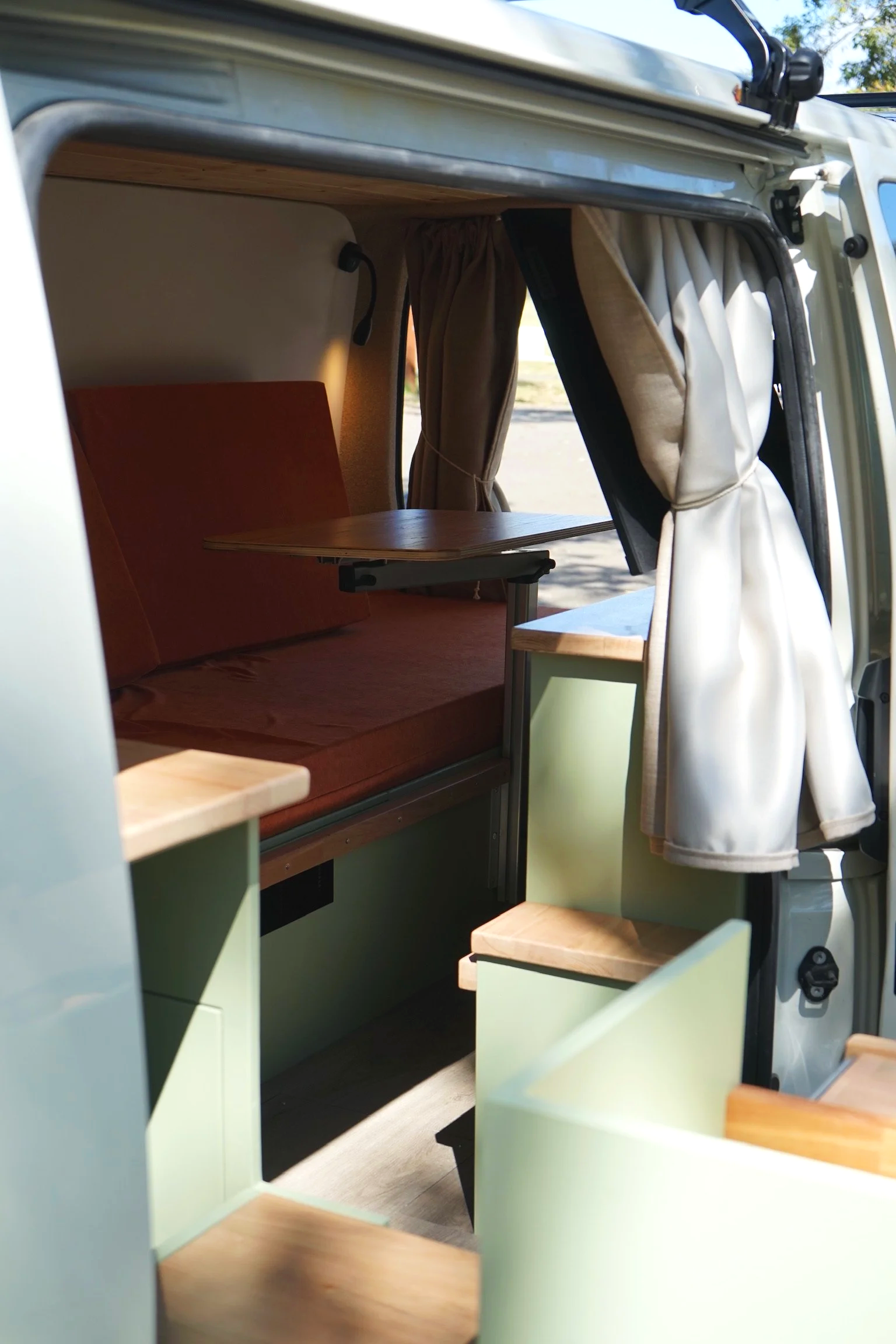Toyota Hiace campervan interior with fold-out table, curtains, timber finishes and custom seating by Amber Fitouts.