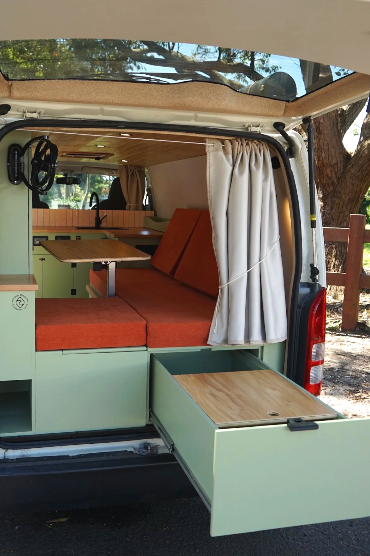 Custom Toyota Hiace campervan conversion with green cabinetry, orange cushions, curtains and pull-out storage by Amber Fitouts in Sydney.