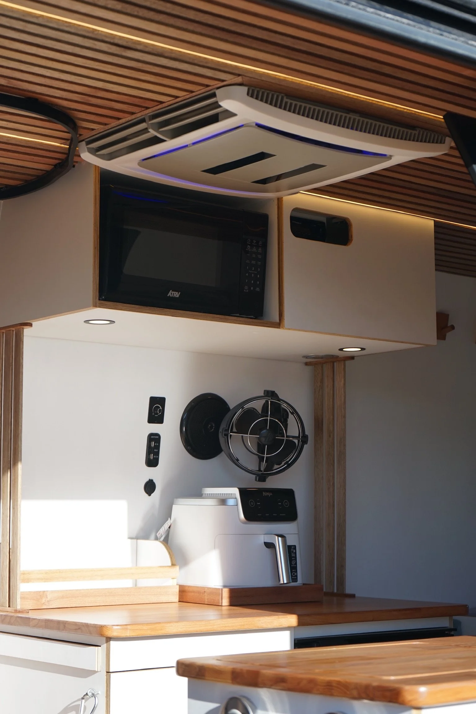 Mercedes Sprinter campervan kitchen interior with timber ceiling, lighting, microwave, fan and custom cabinetry