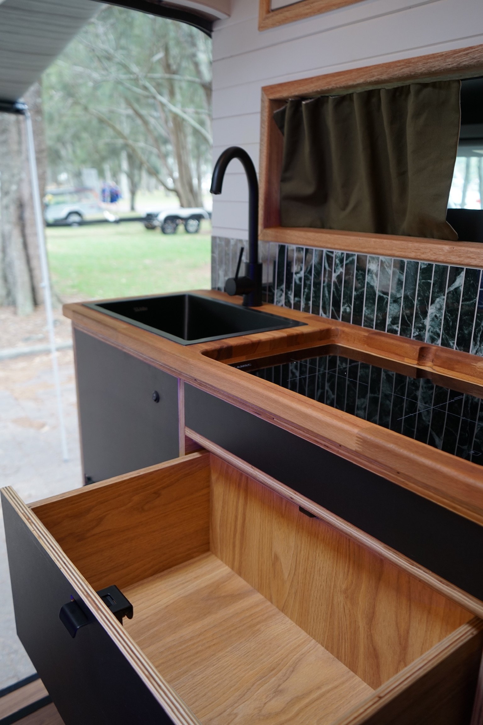 Ford Transit campervan kitchen with timber benchtop, sink, custom cabinetry, storage drawer and tiled splashback