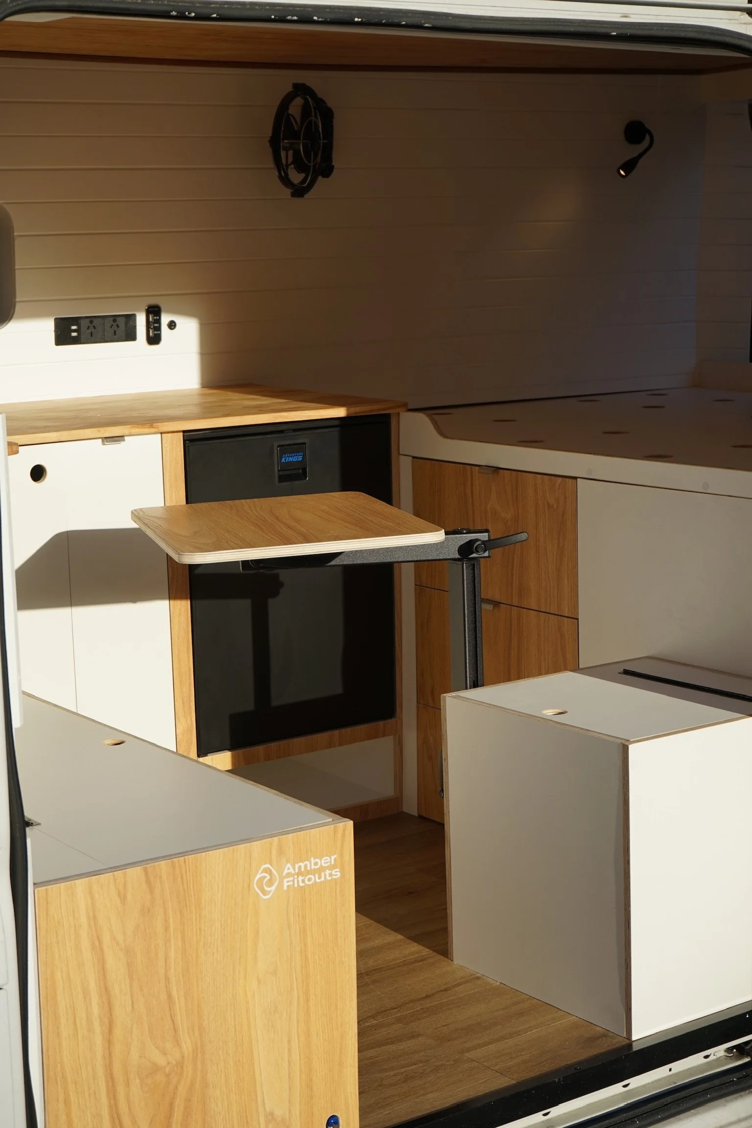 Fiat Ducato campervan kitchen and storage layout with fridge, pull-out table, timber cabinetry and open floor space.