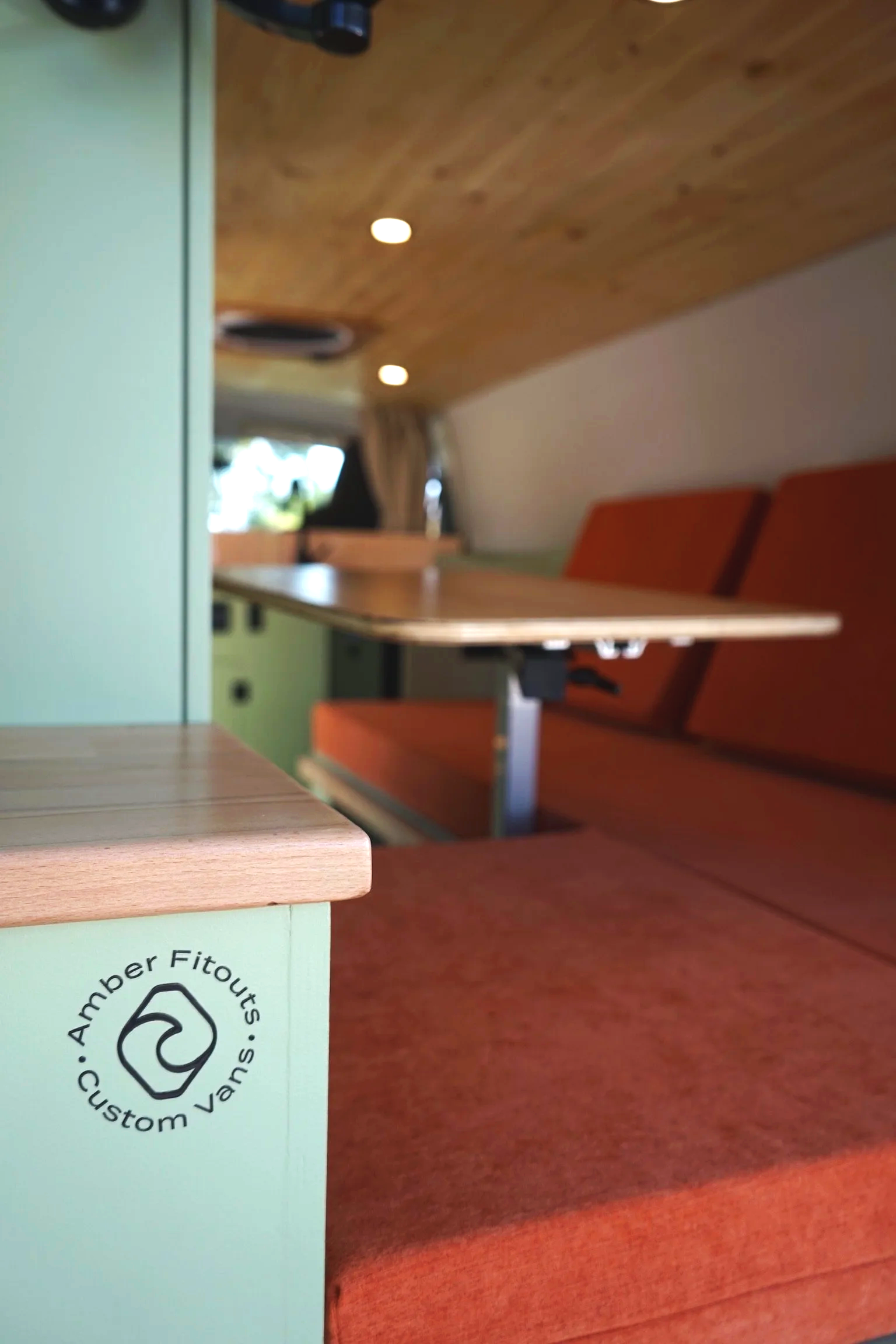 Toyota Hiace LWB campervan interior with orange upholstery, fold-out table, timber ceiling and custom cabinetry.