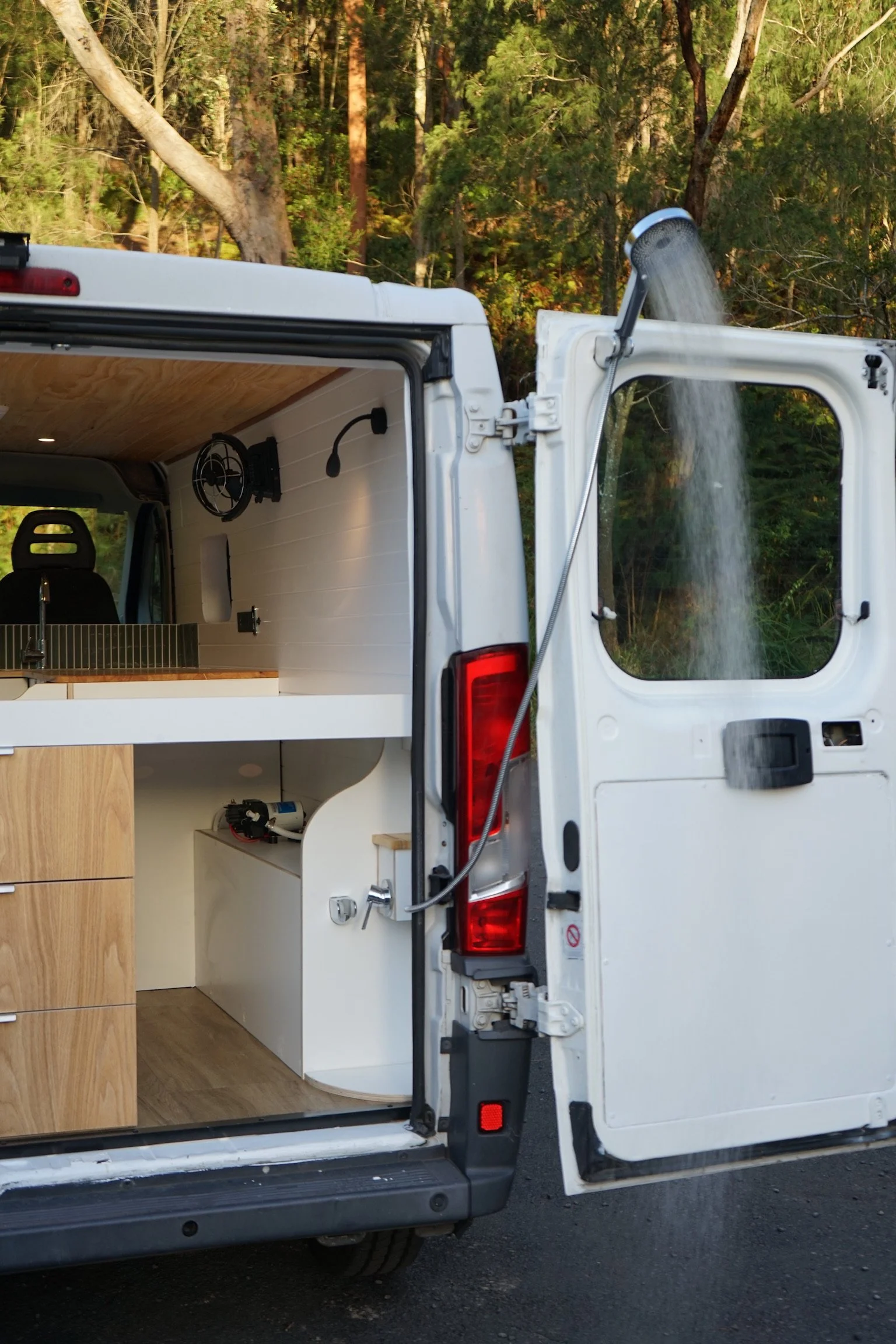 Fiat Ducato campervan interior with shower area, timber cabinetry, drawers, fan and warm lighting