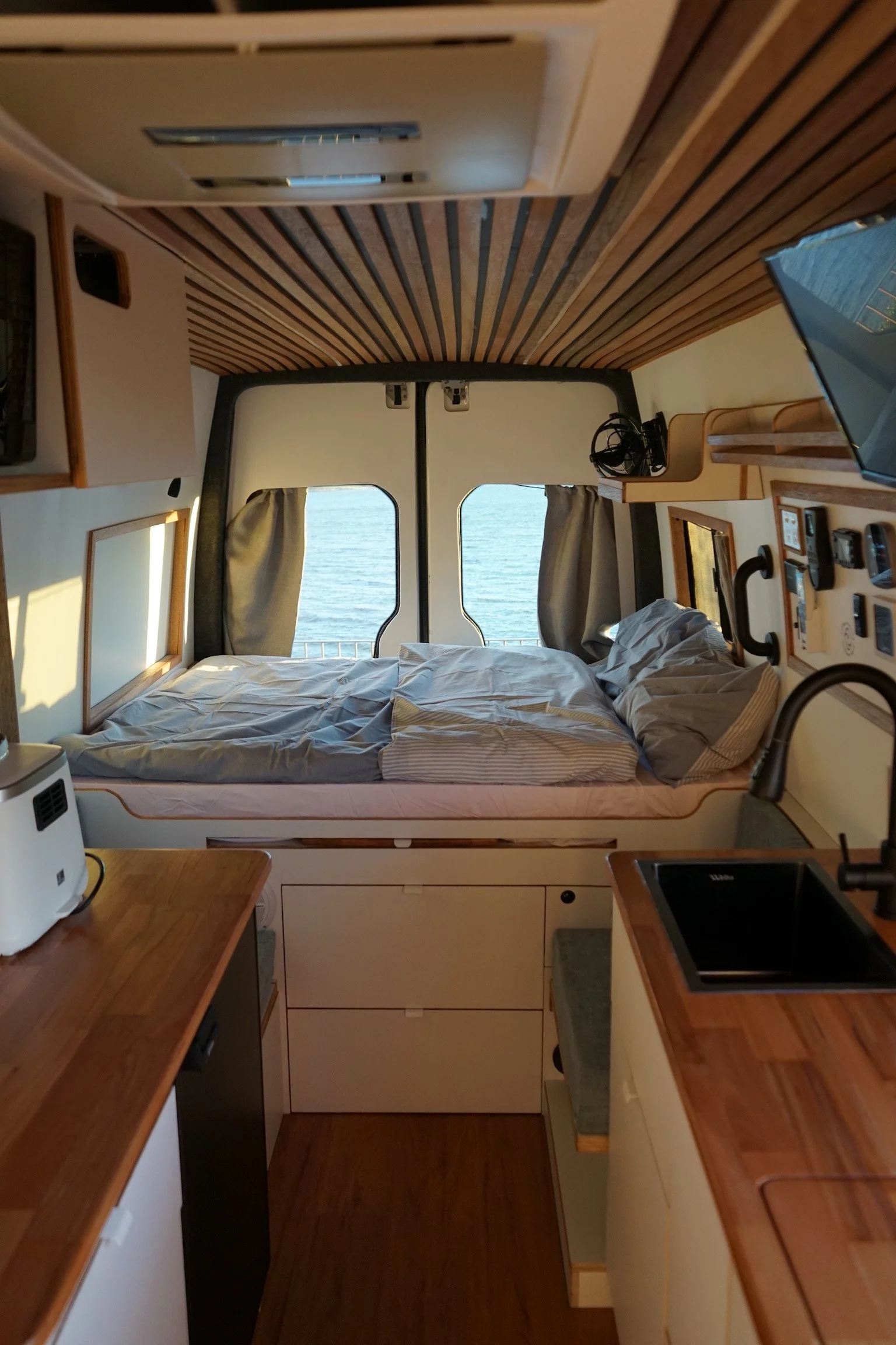Mercedes Sprinter LWB campervan layout with bed, kitchen benches, sink and timber ceiling by Amber Fitouts.
