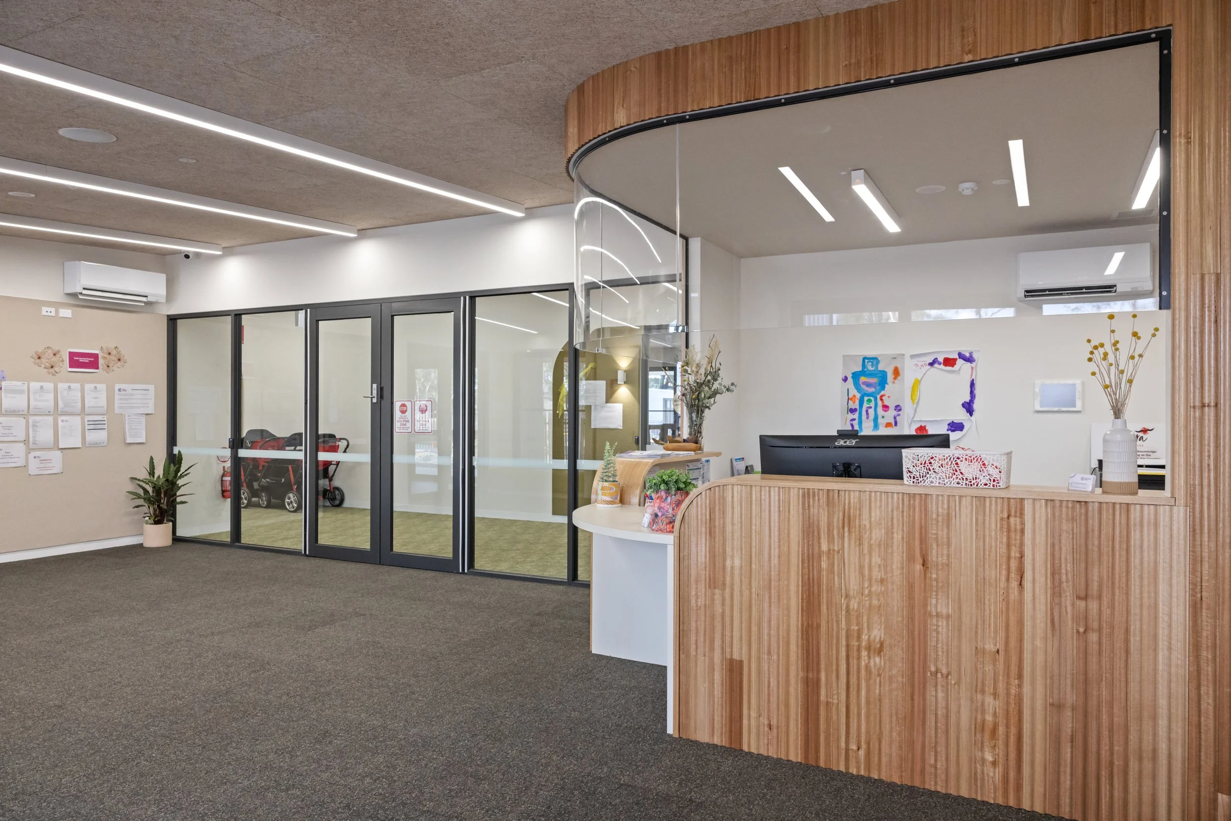 Reception area with wooden curved accent wall, glass door, colorful artwork, and decorative plants.