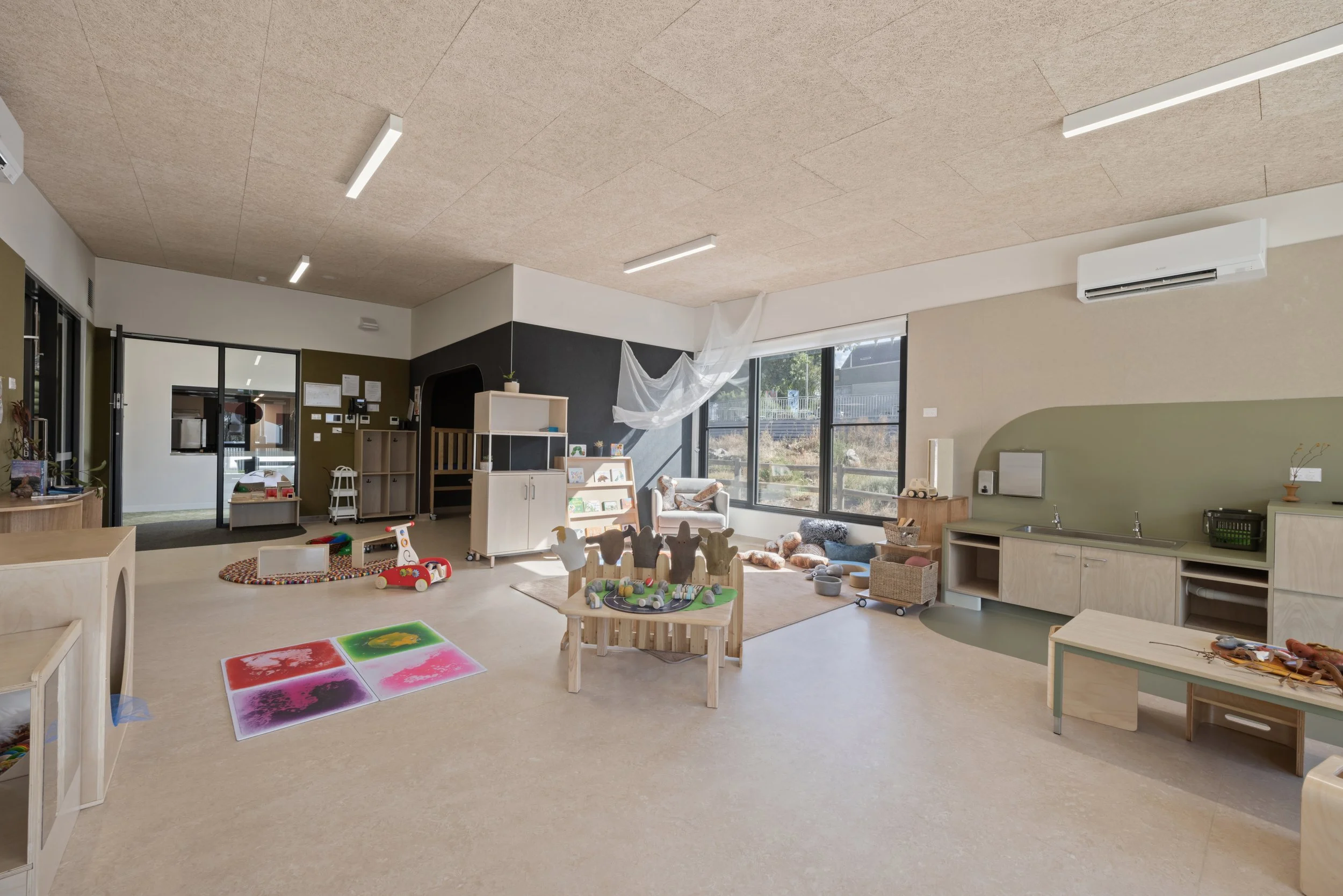 Interior of a children's playroom with toys, furniture, and large windows allowing natural light.