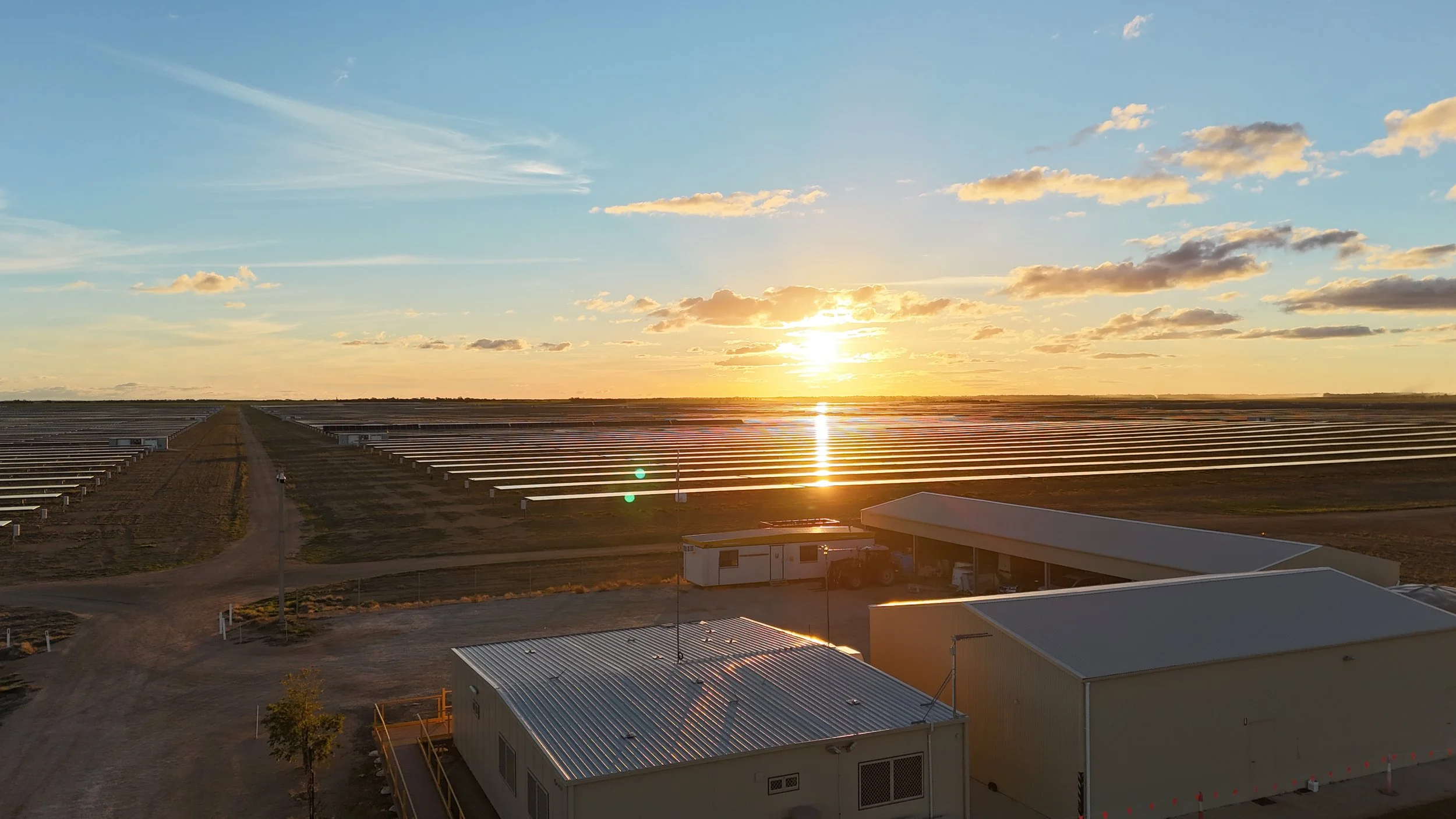 Sunset over a solar panel farm with buildings in the foreground.