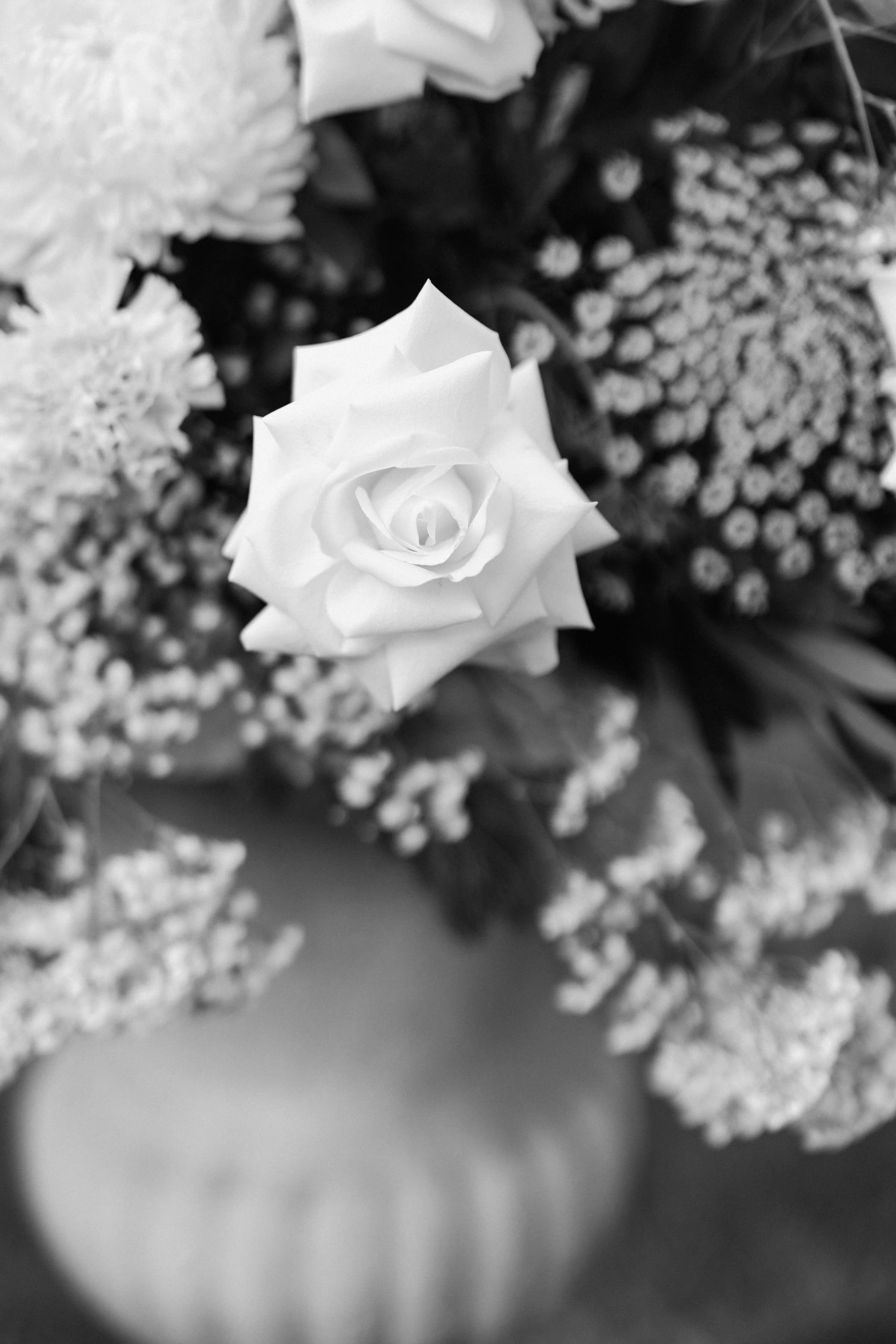 A white rose surrounded by smaller flowers in a bouquet, captured in black-and-white.