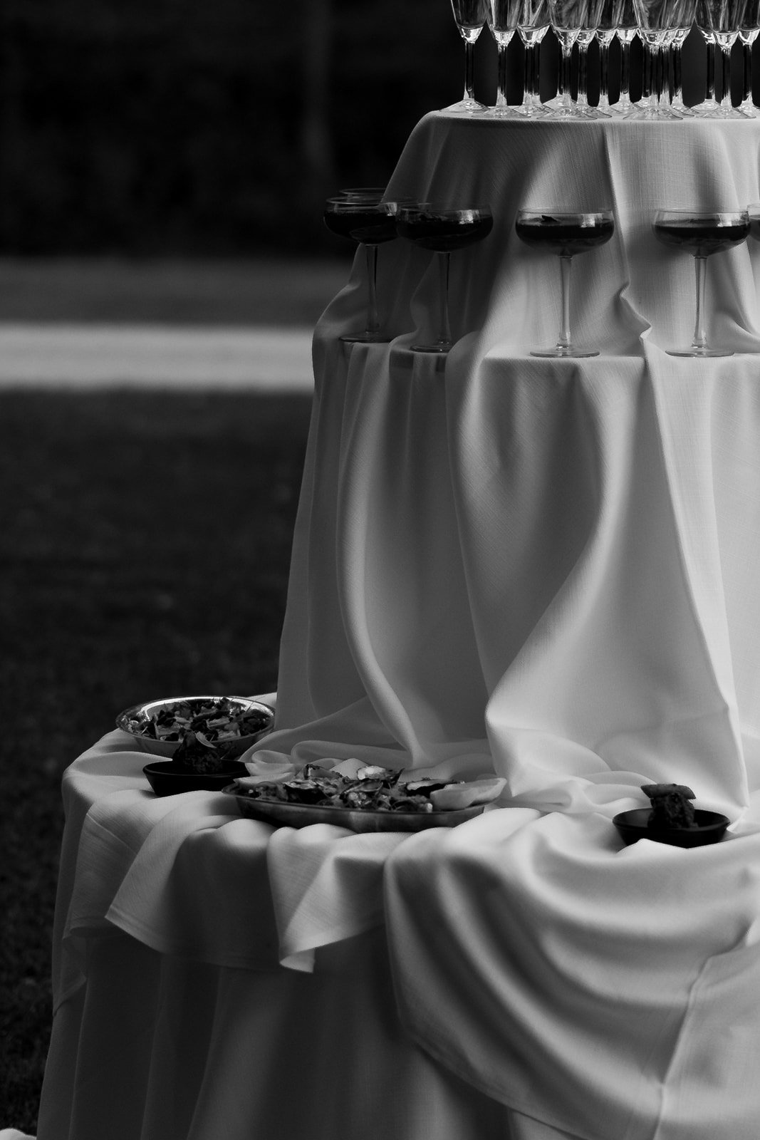 Table with a white cloth, holding empty wine glasses on top, and food dishes with appetizers or snacks on the lower part.