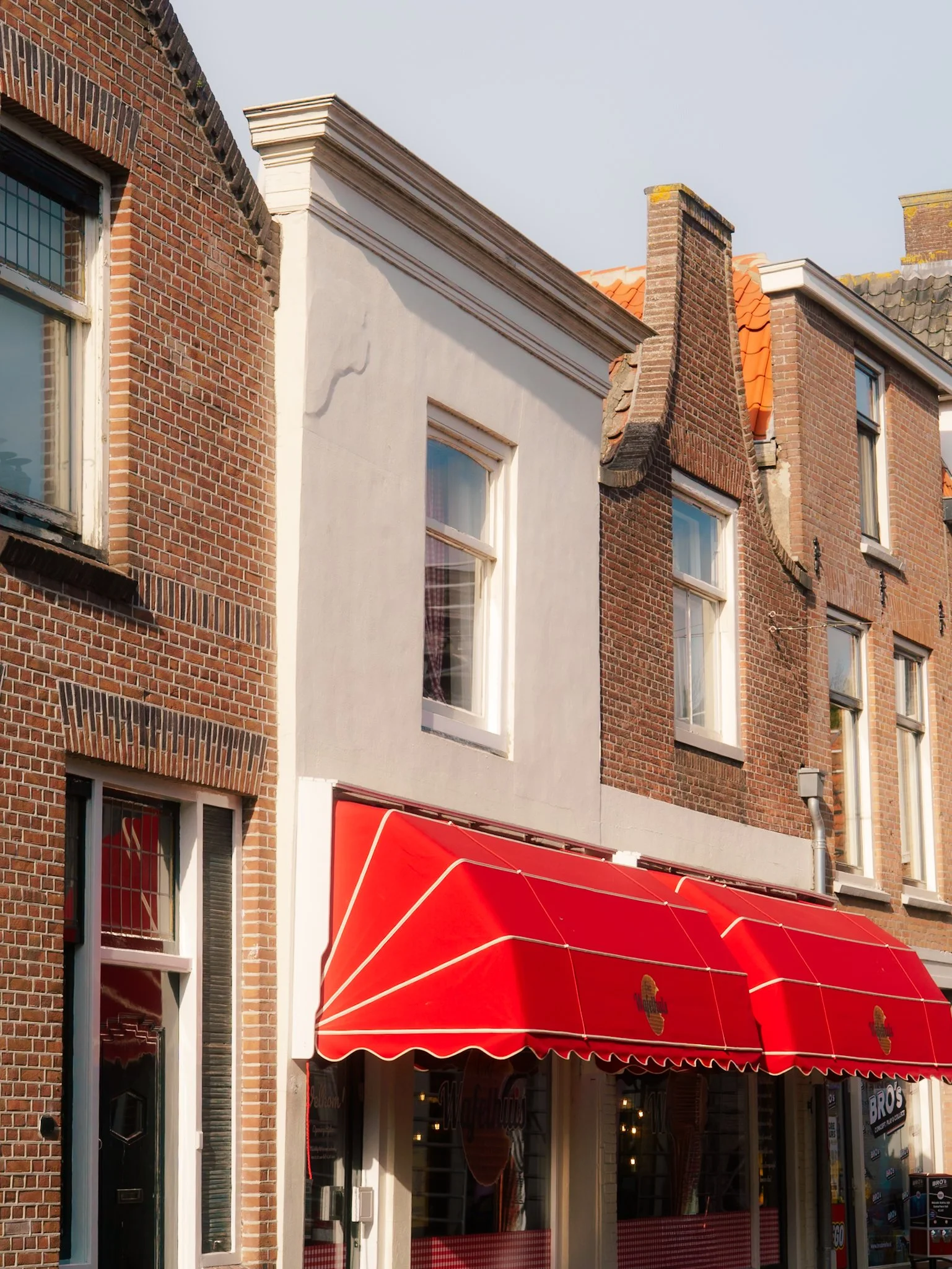 De gevel van een gebouw met een aantrekkelijk rood-wit betegeld winkelruit en een rode parasol in de voorkant.
