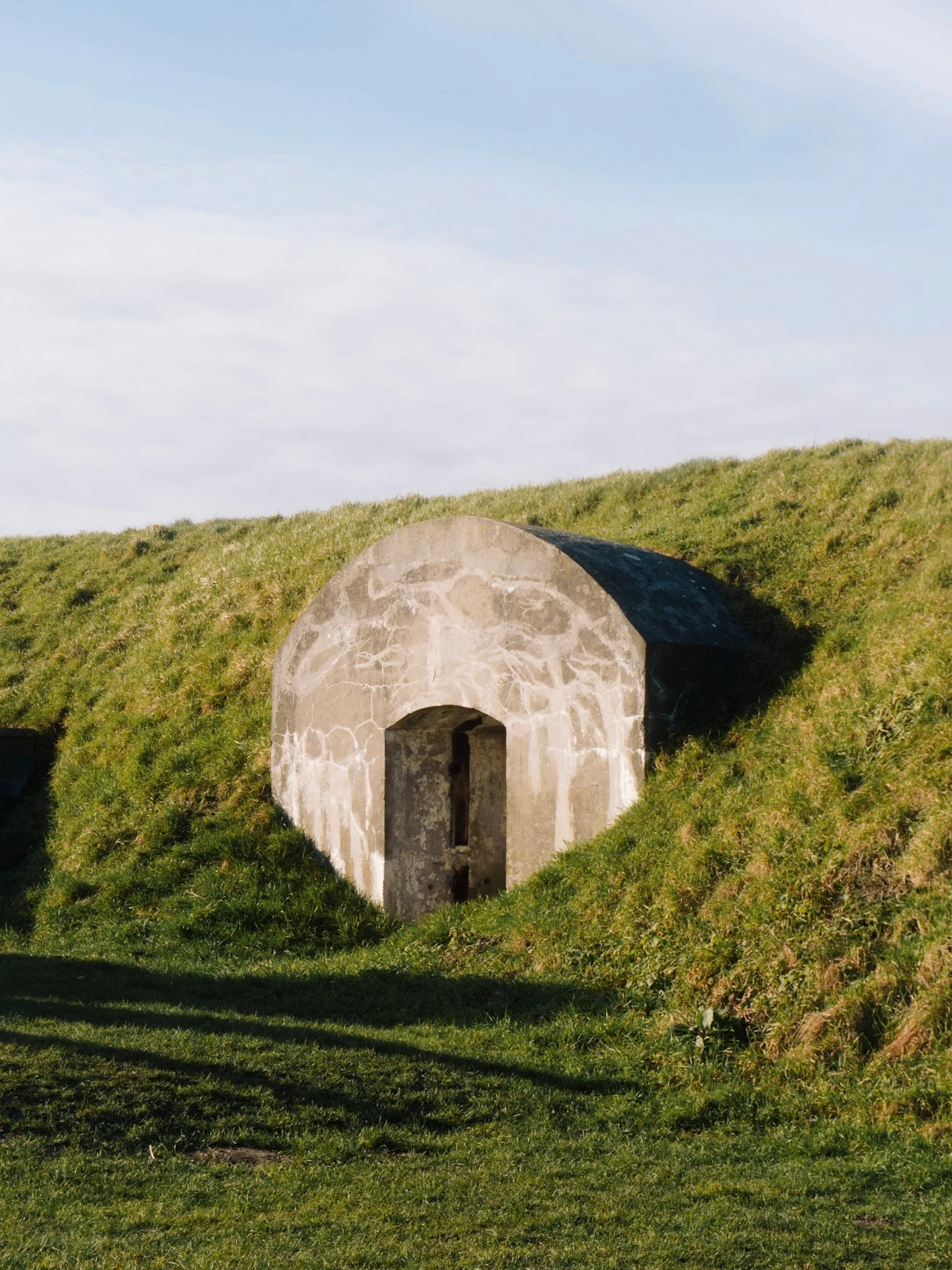 Een klein burchtachtig gebouw met een arched ingang, gelegen op een grasveld met heuvels en een heldere hemel op de achtergrond.