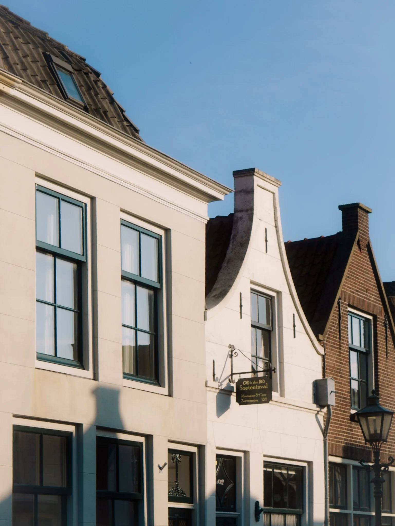 Gezicht op de gevels van meerdere huizen met verschillende dakranden en ramen, onder een blauwe hemel.