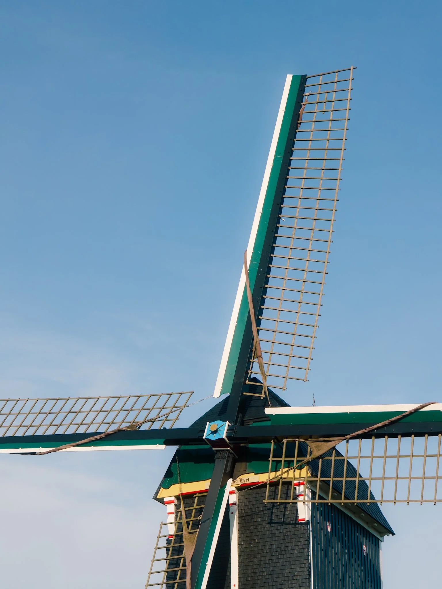 Traditionele Nederlandse windmolen met draaiende wieken tegen een heldere blauwe hemel.