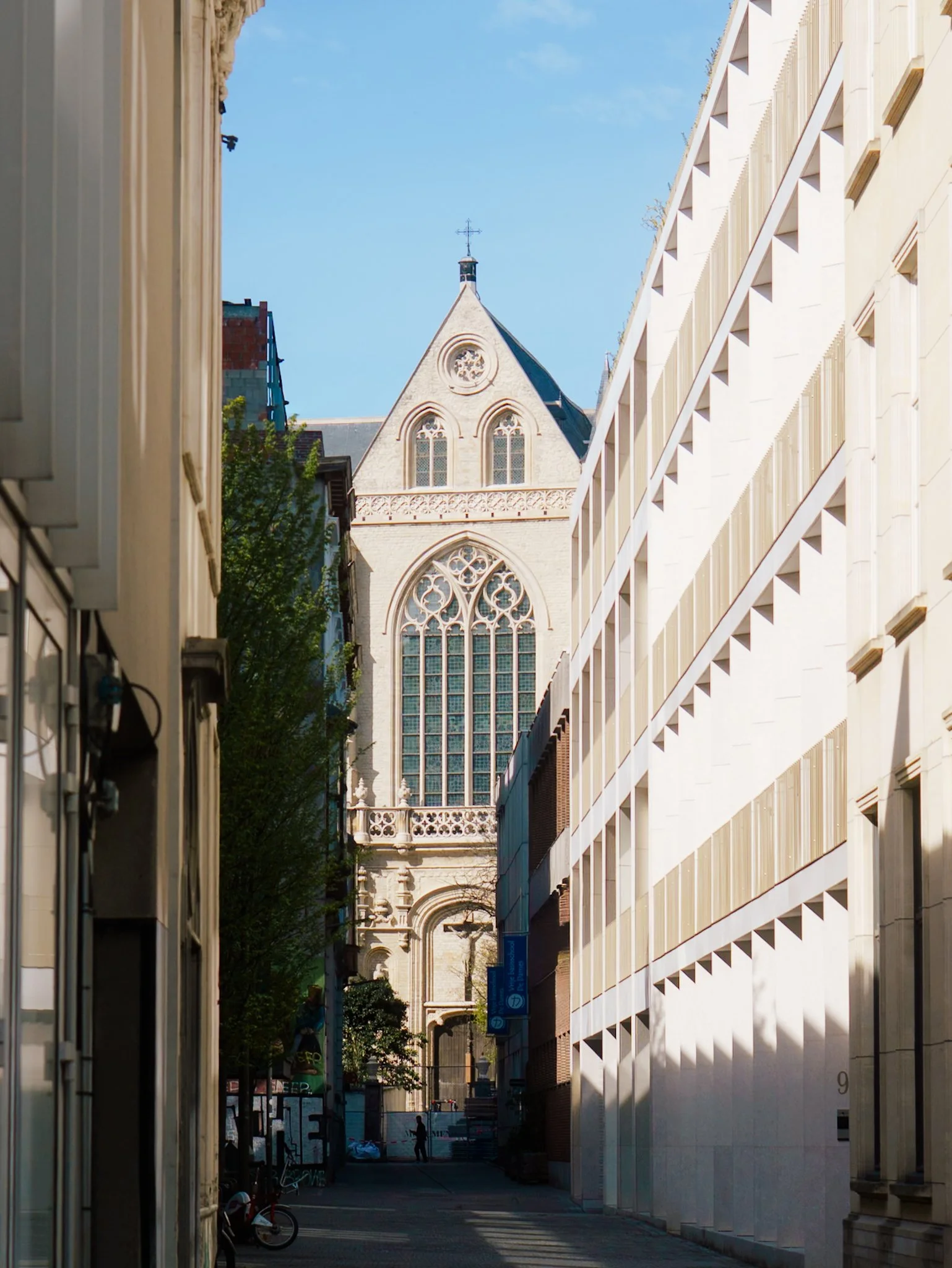 Een smalle straat tussen moderne gebouwen met grote ramen en een historische kerk op de achtergrond.