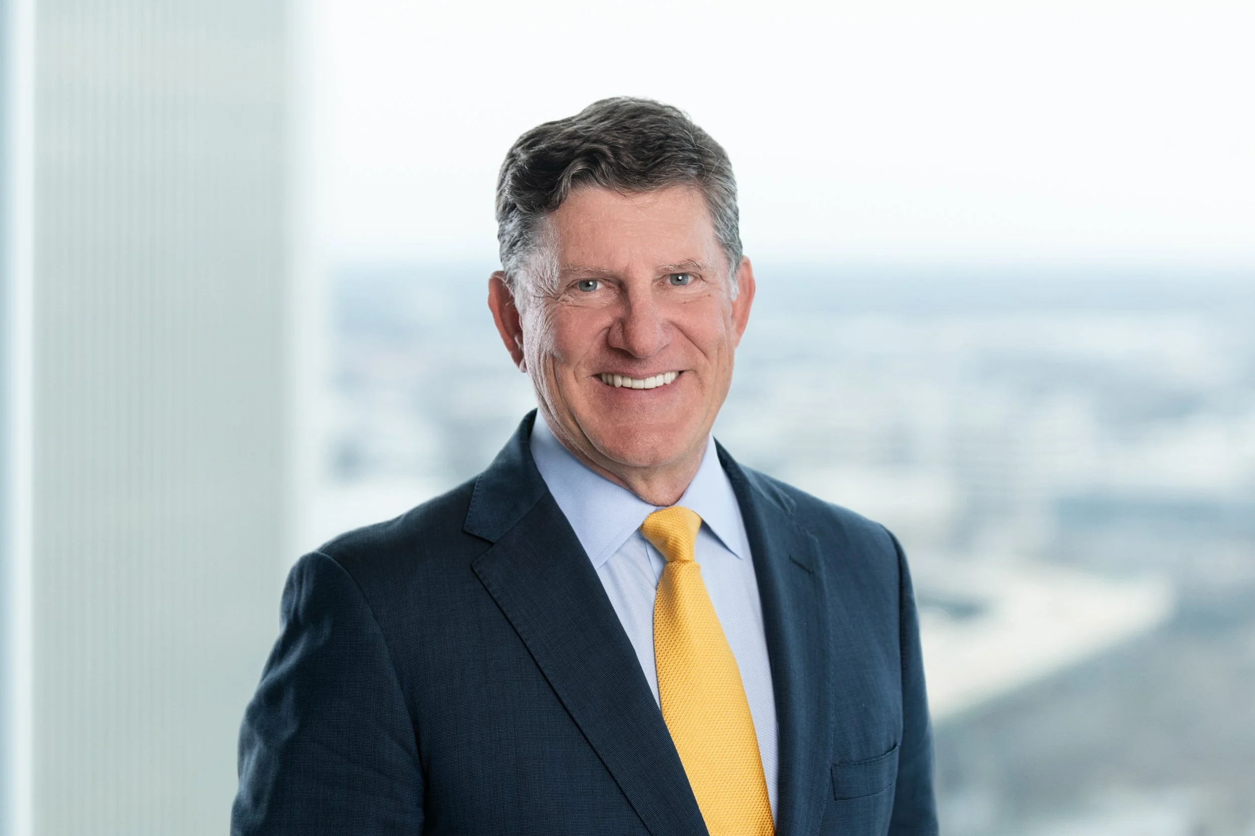 Professional man in suit smiling in an office with a city view background.