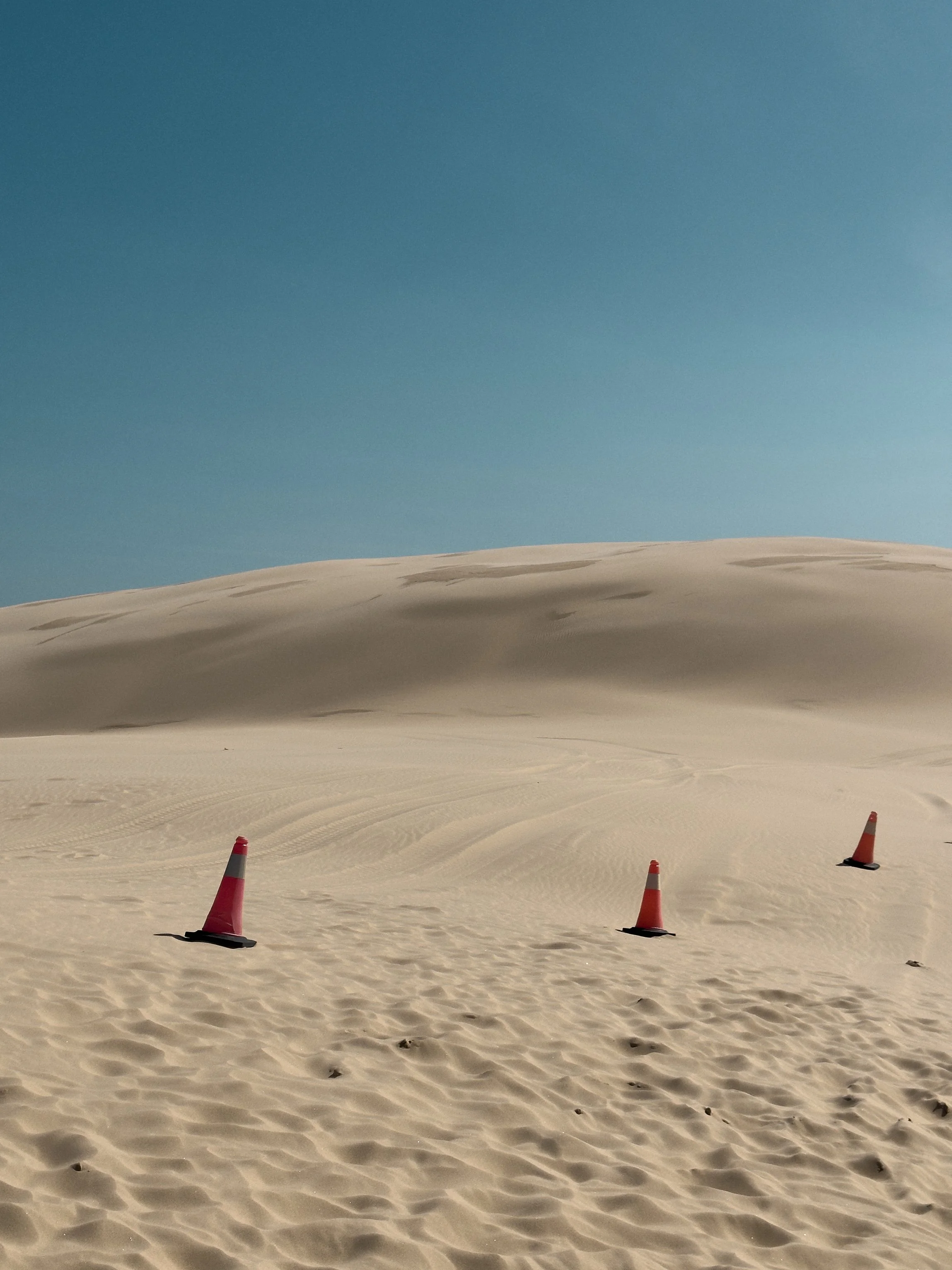 3 traffic cones on sand dunes with blue sky
