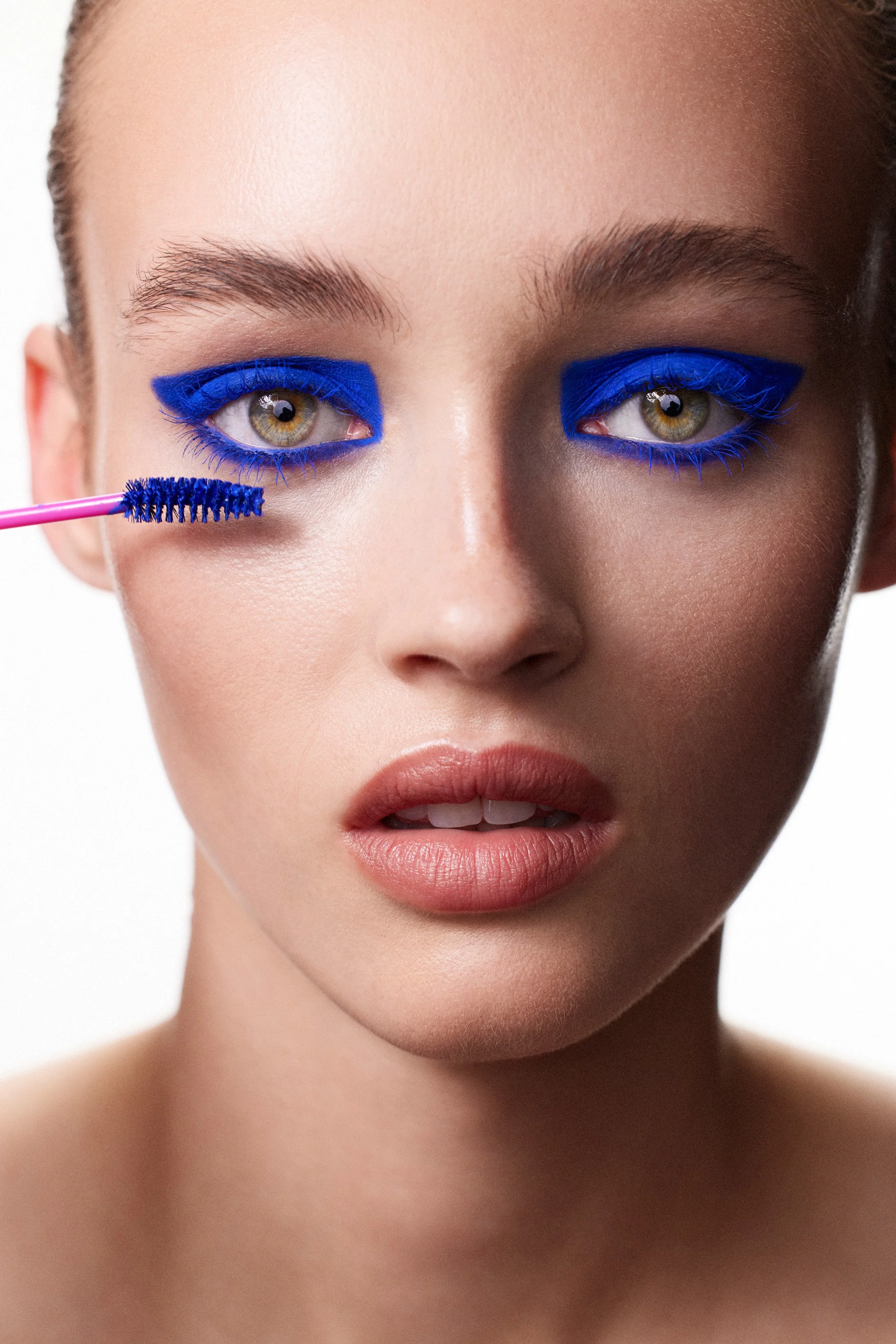 A beauty portrait of a female model with blue eyeliner being applied by a pink brush