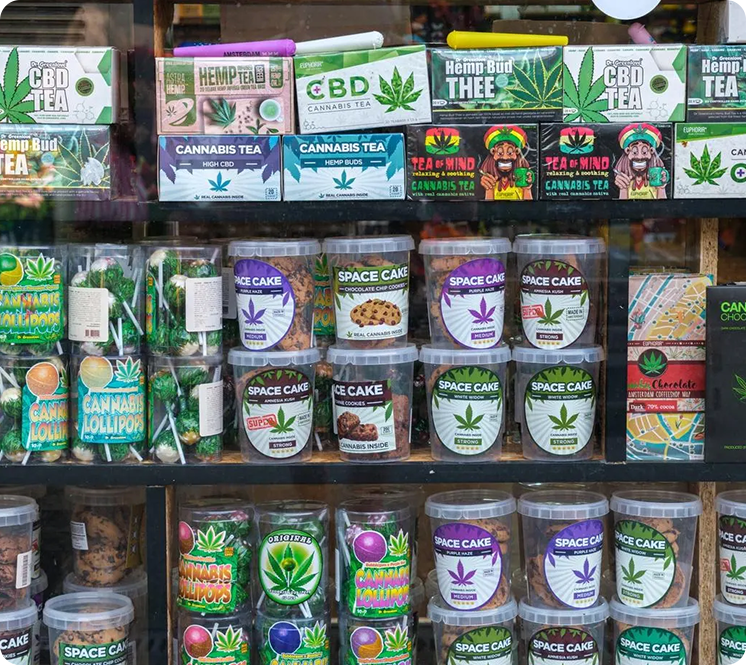 Display of various cannabis-themed tea, candies, and cookies on store shelves, including hemp tea, CBD tea, space cake cookies, and cannabis lollipops.