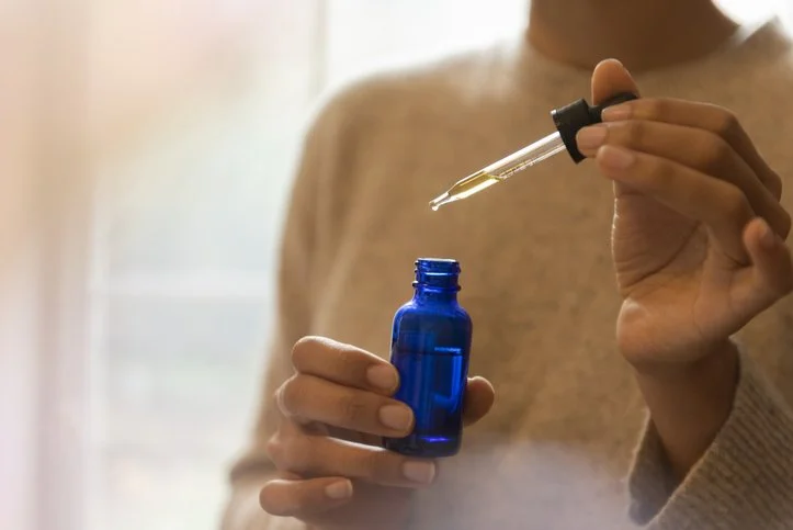 Person holding a small blue glass bottle and using a dropper to extract liquid from it.