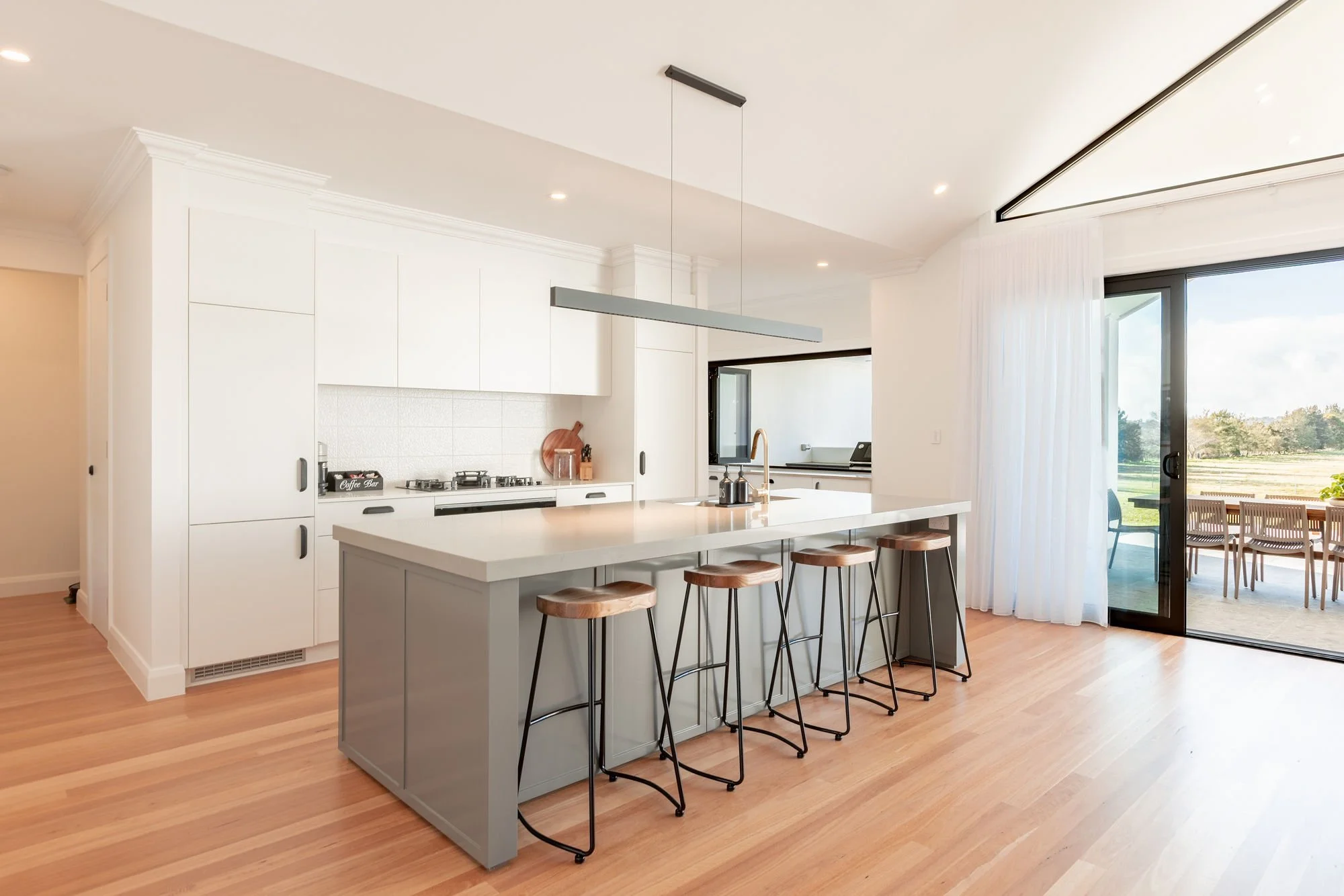 Modern kitchen with white cabinetry, island with seating, and sliding glass door leading to outdoor dining area.