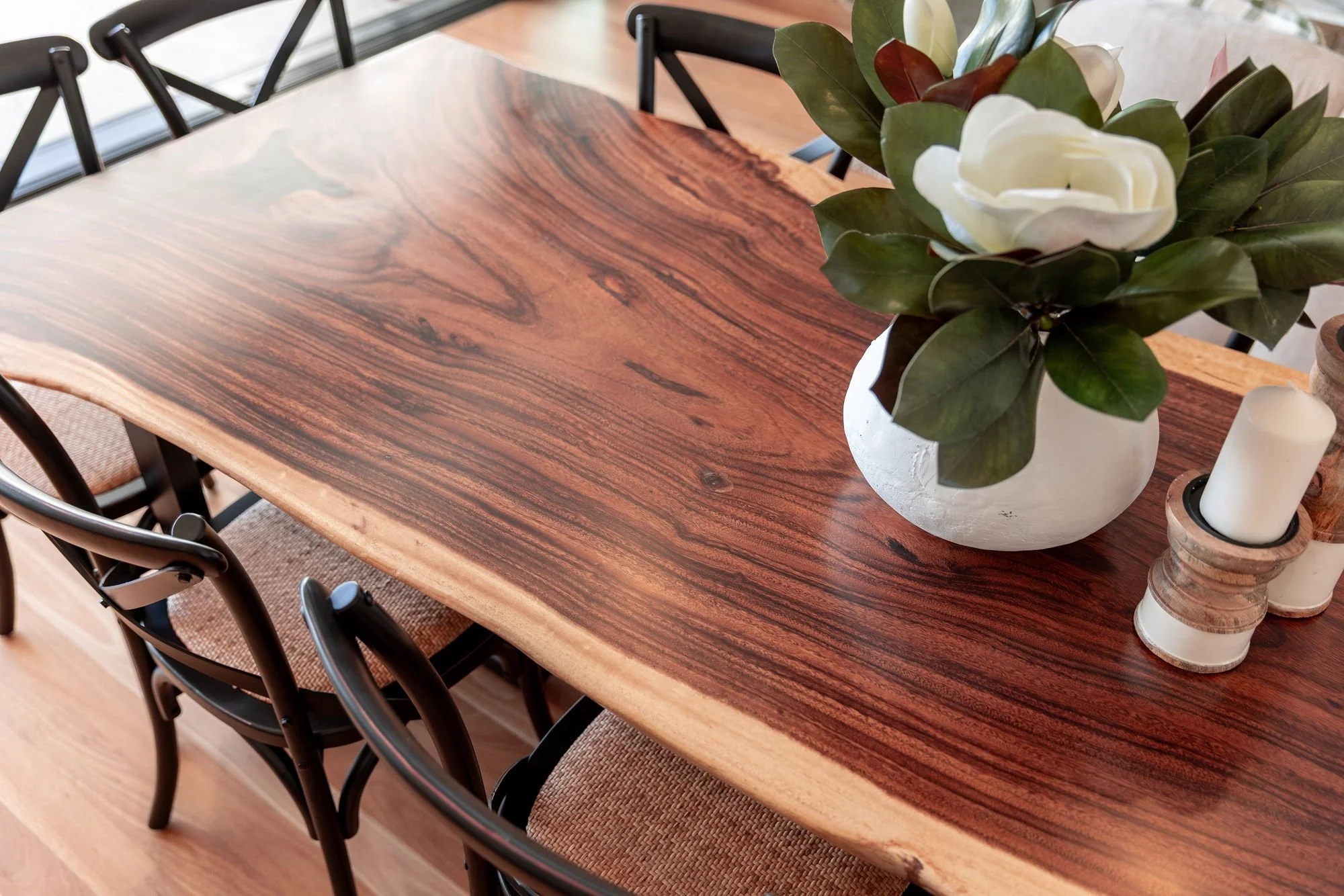Wood dining table with a white vase holding a large magnolia flower, green leaves, and candles.