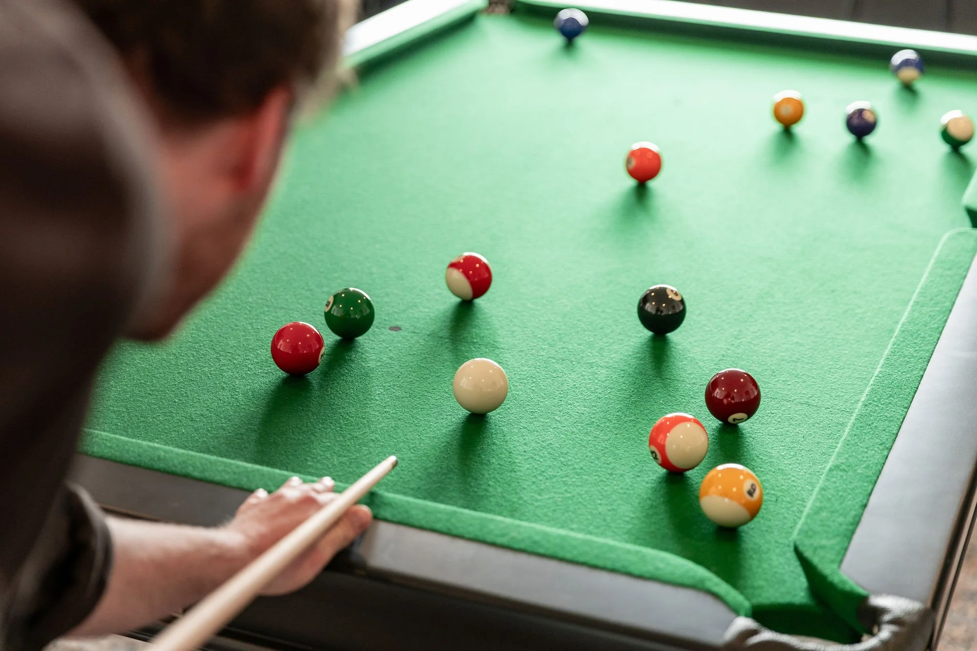 Person playing billiards on a green felt table with various pool balls scattered across the surface.