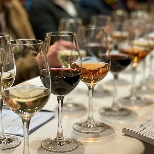 A row of wine glasses filled with various types of wine, held by people at a tasting event.