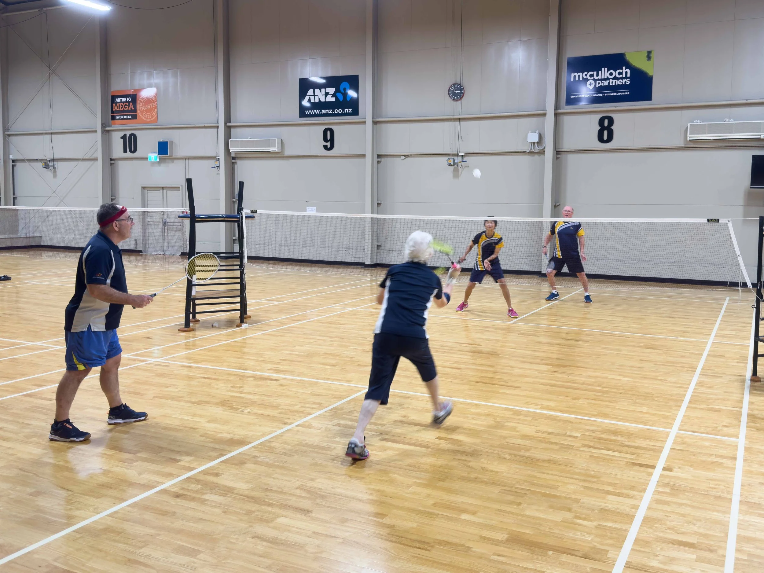 Group of people playing badminton in an indoor gymnasium.
