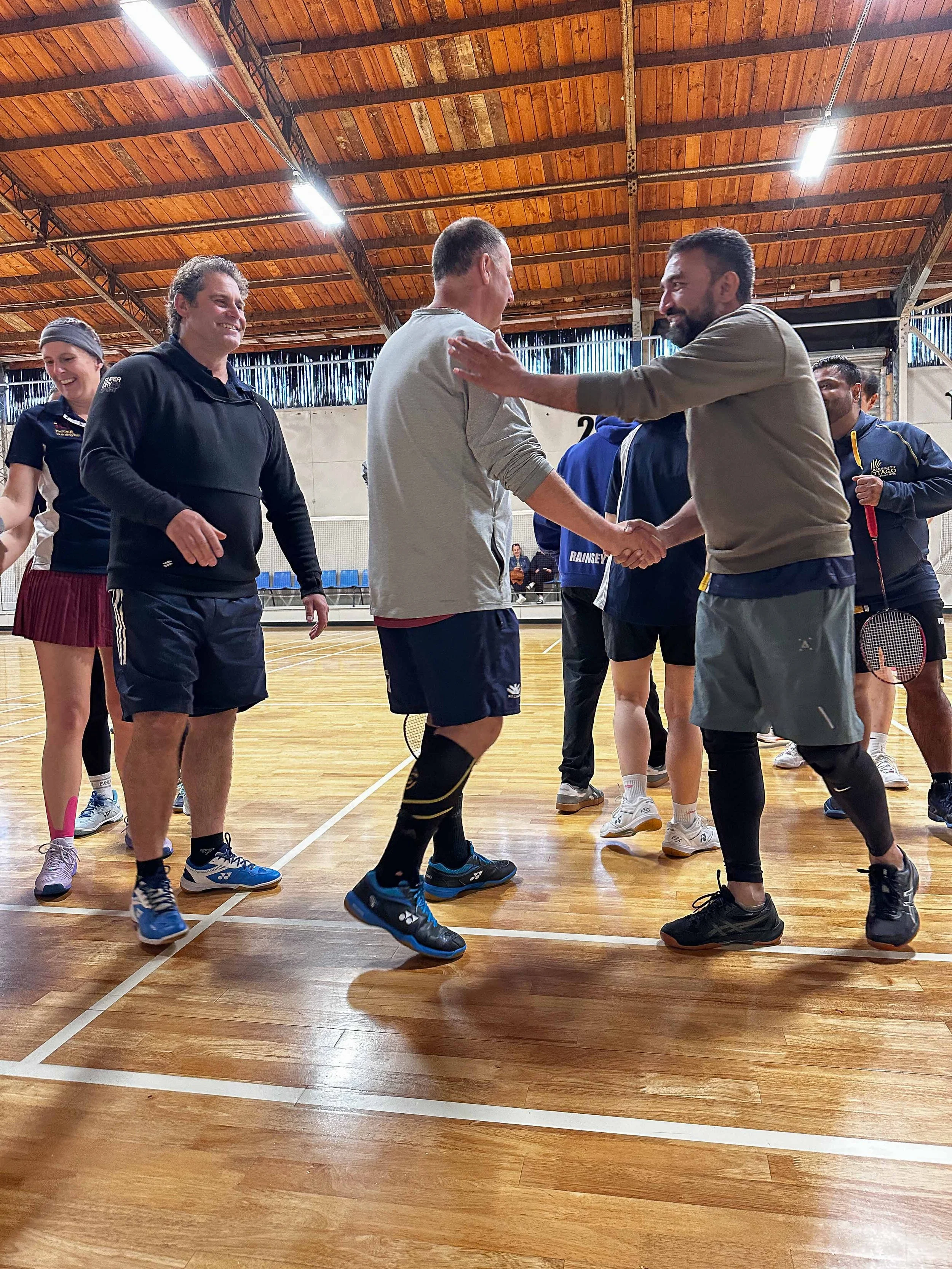 People in a gymnasium shaking hands and smiling after playing badminton.