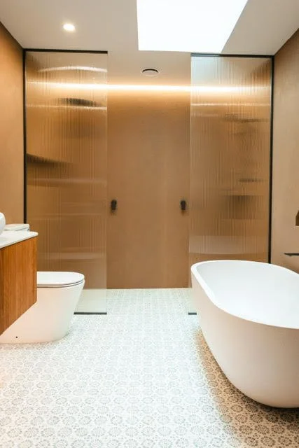 Modern bathroom with a freestanding bathtub, toilet, wooden vanity, and metallic sliding doors.