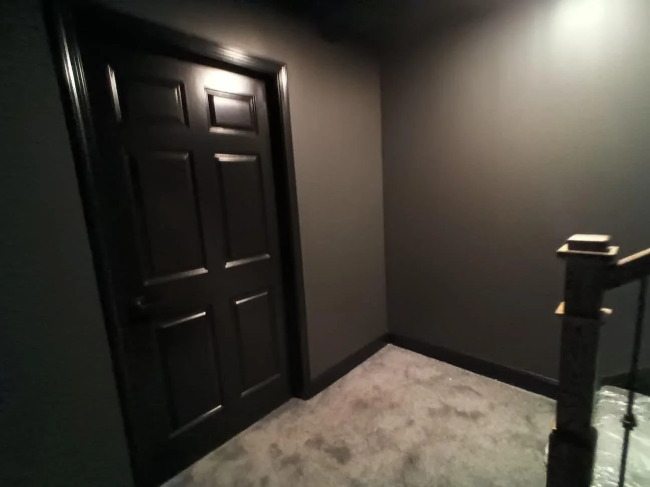 Dark hallway corner with a closed black door and a staircase bannister on the right.