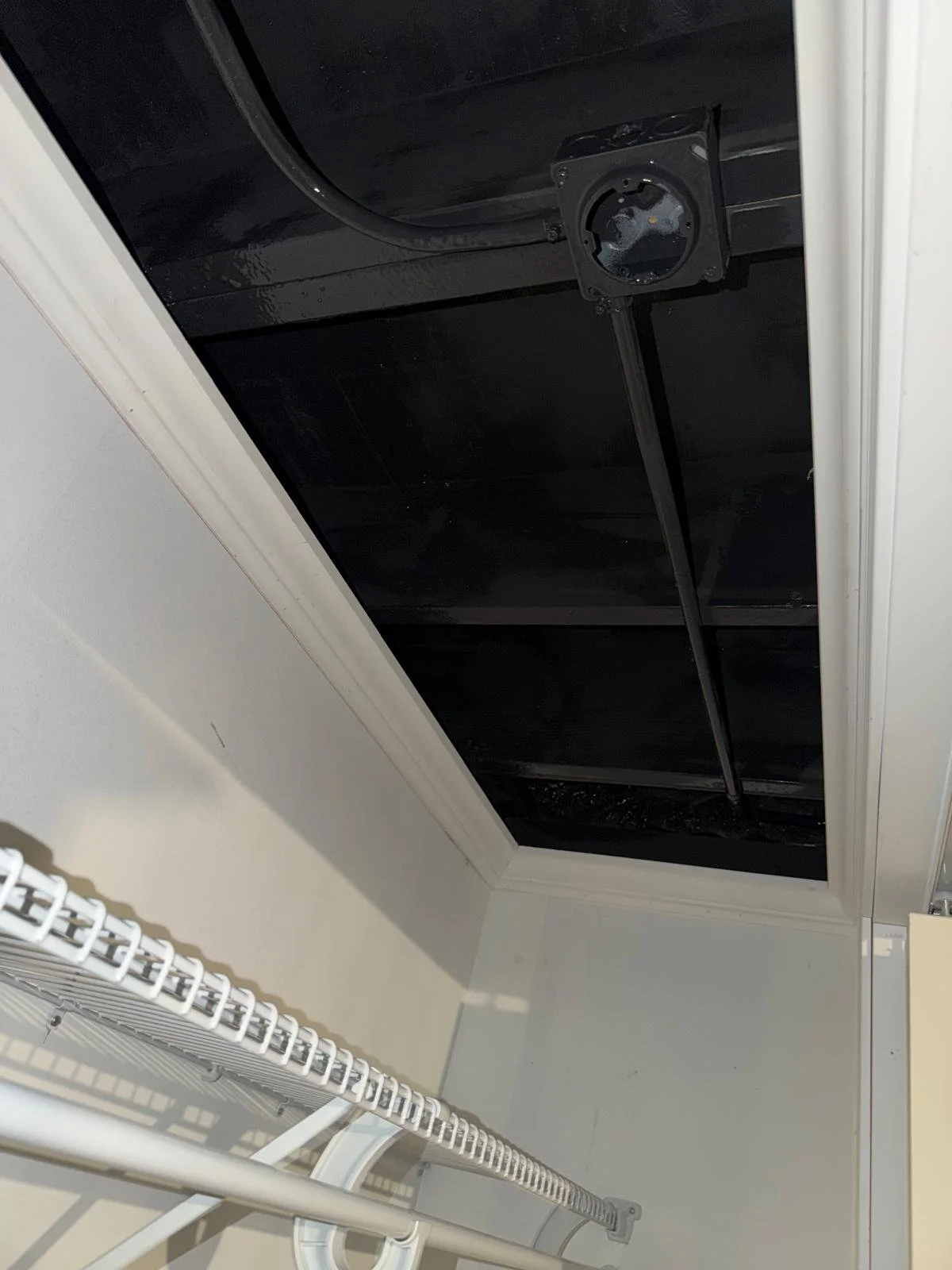 Empty closet with black ceiling, white walls, white wire shelf, and rod for hanging clothes.