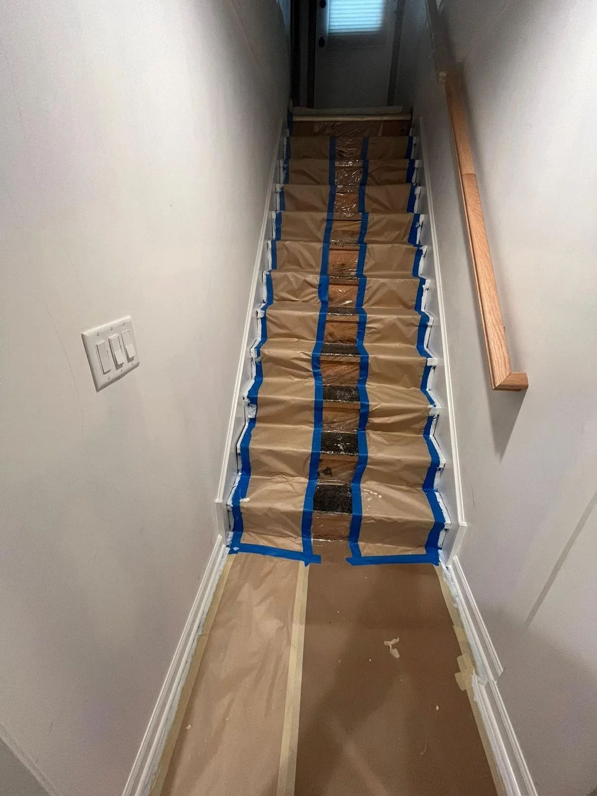 A staircase covered with brown paper and blue painter's tape, indicating ongoing repairs or renovation.