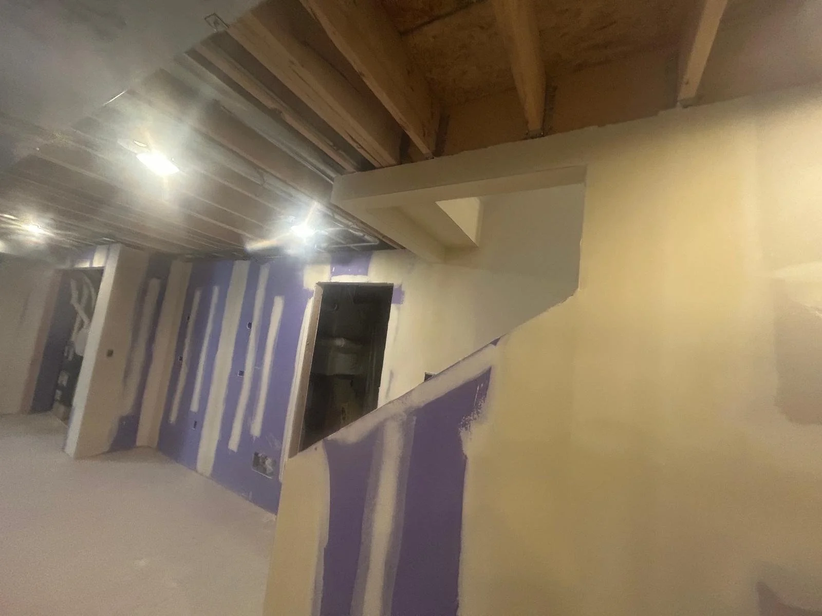 Interior of a house under construction with partially painted walls, exposed wooden ceiling, and construction lights.