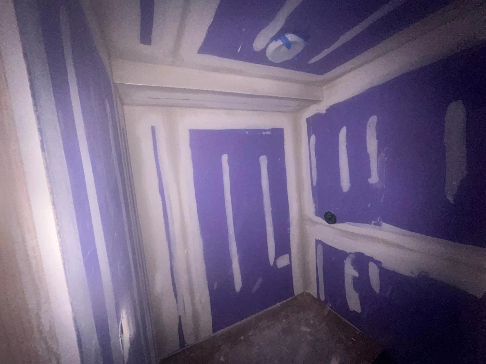 A room with purple drywall panels and white joint compound applied to seams and screw holes, indicating ongoing drywall installation or finishing.