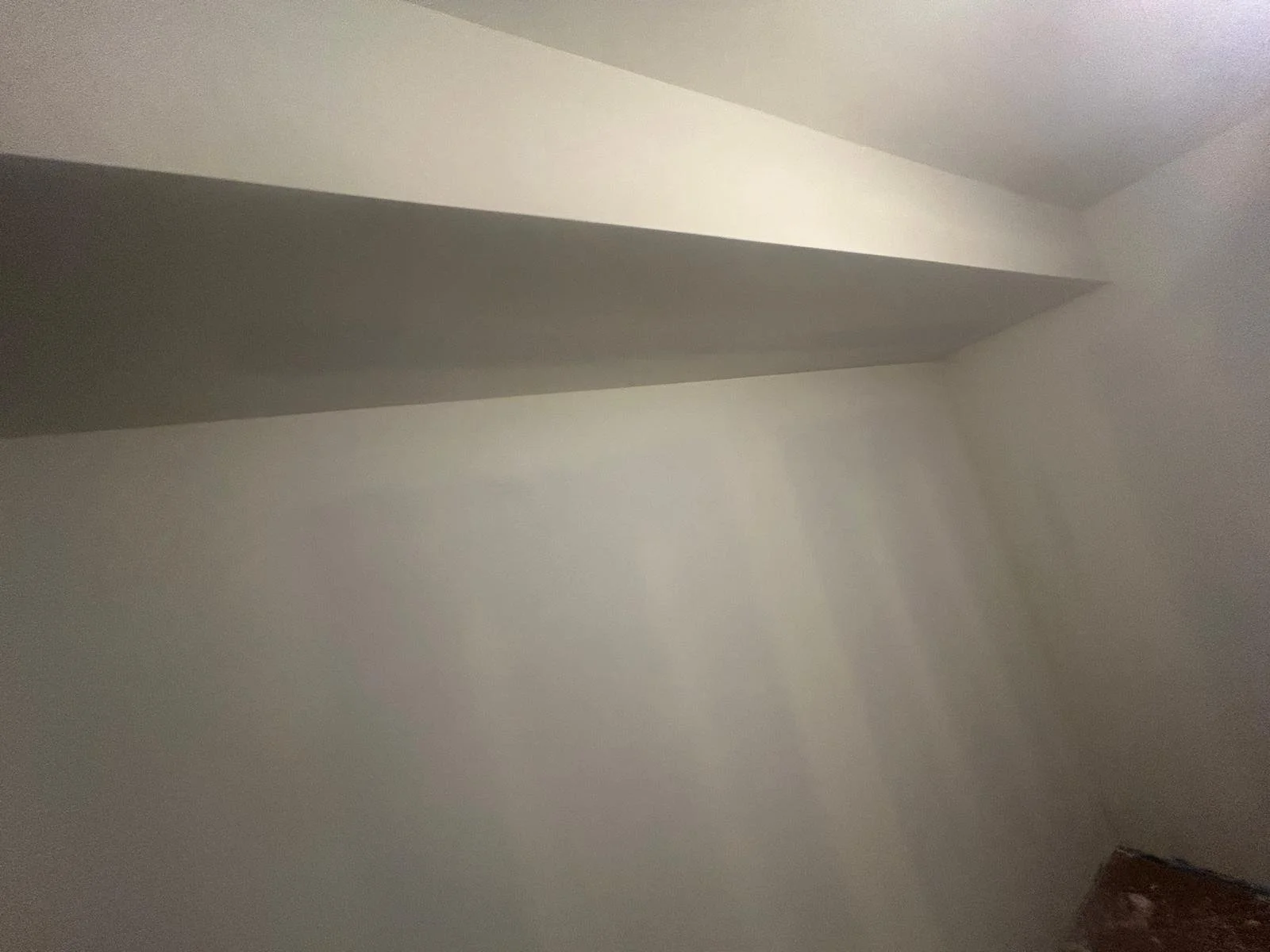 Empty room with plain white walls and a ceiling, with a corner and a small portion of a wooden floor visible in the bottom right corner.