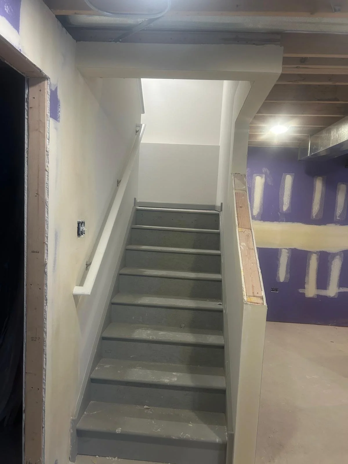 Finishing staircase construction, with painted gray steps and partial wall and ceiling paint, in a home under renovation.