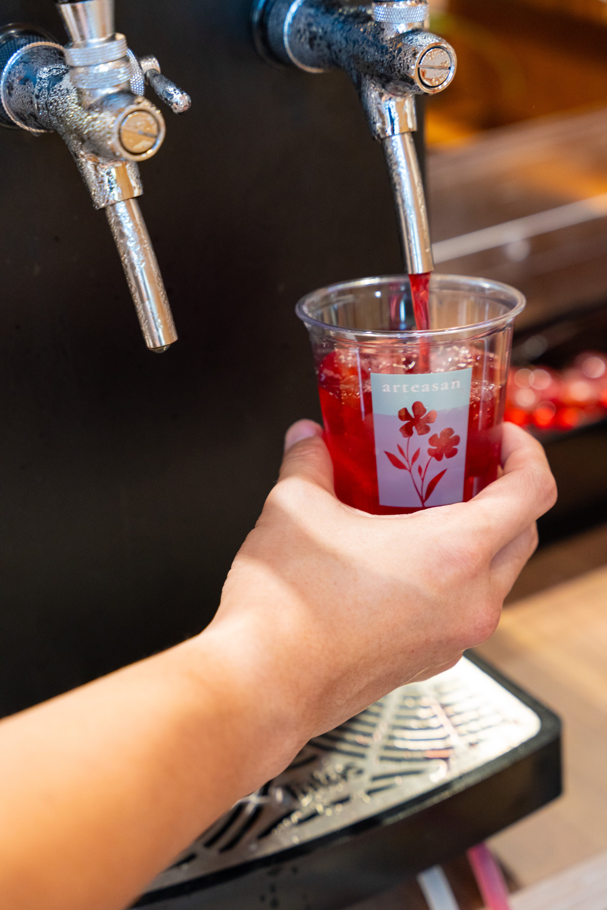 Person filling a clear plastic cup with red juice from a tap at a drink station.