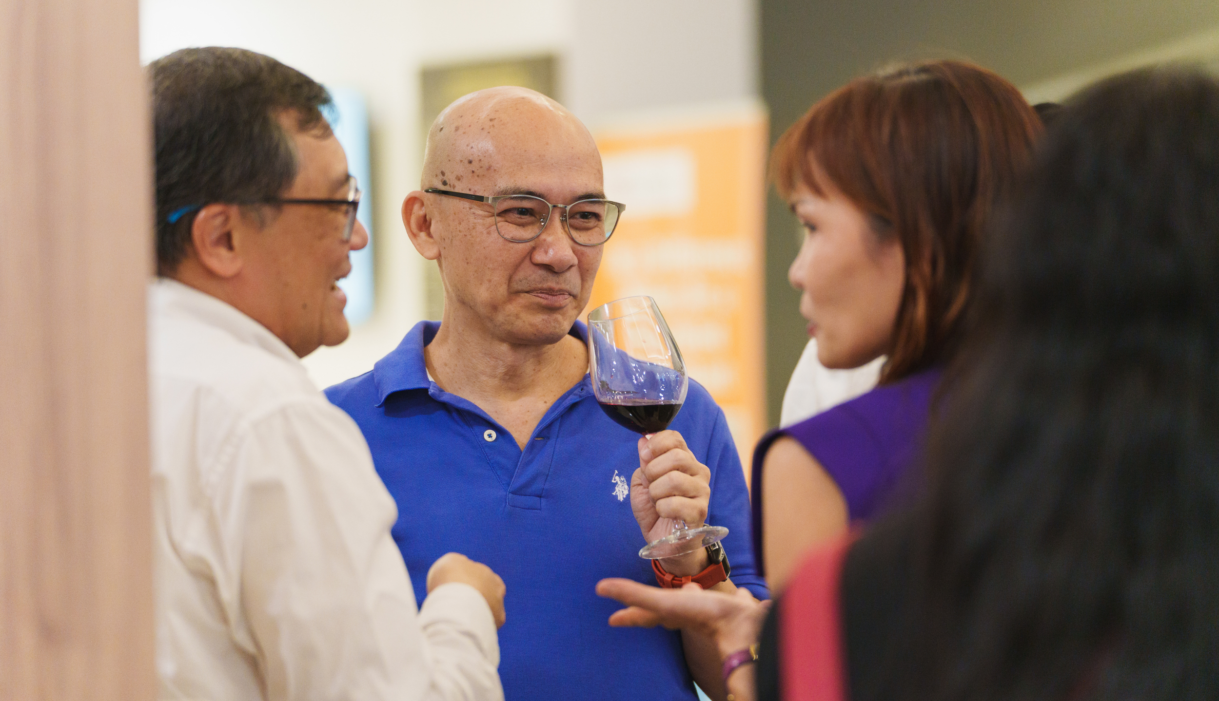 Four people socializing indoors, one holding a glass of red wine, engaging in conversation.