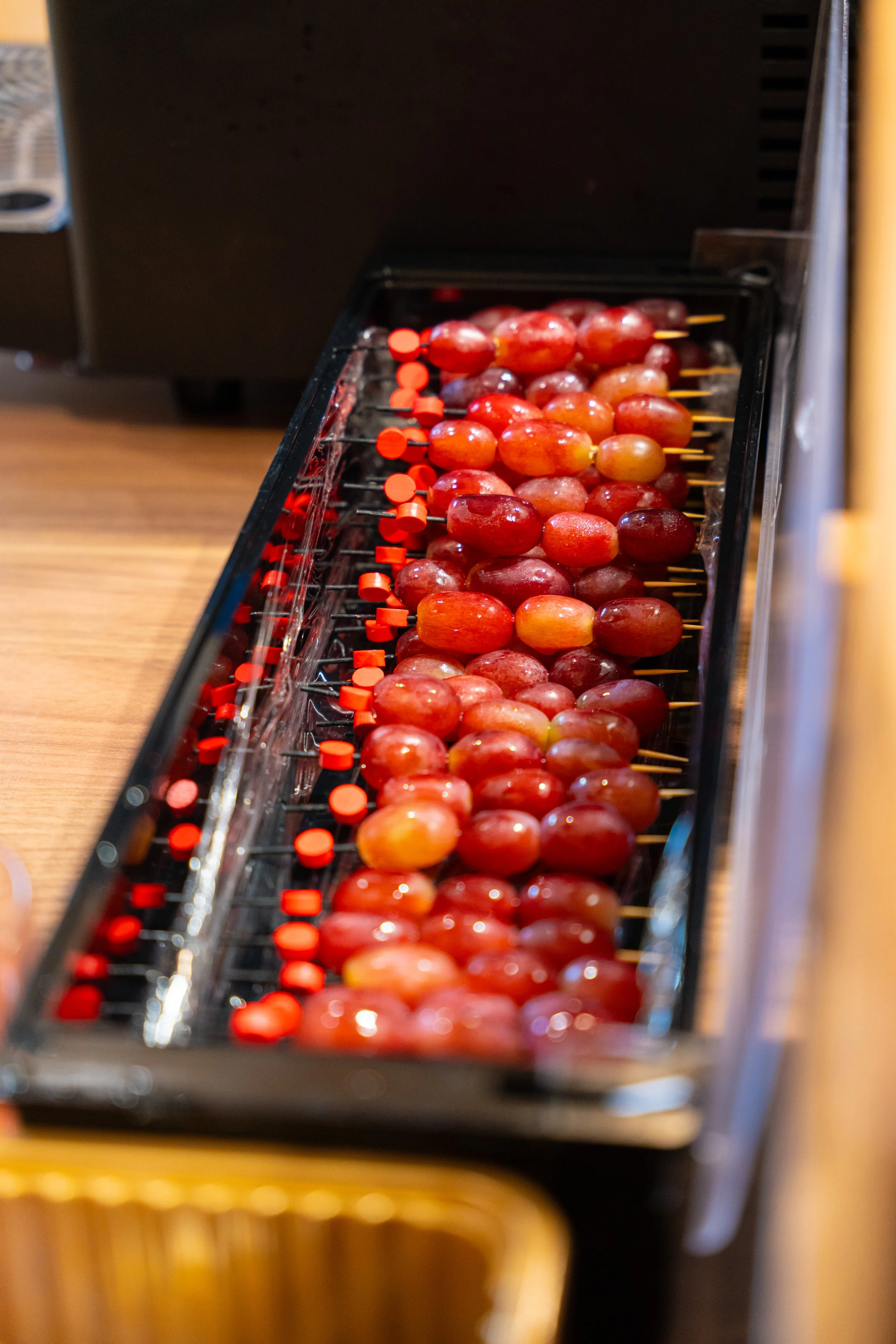 A row of red and purple grapes on skewers inside a glass display case.